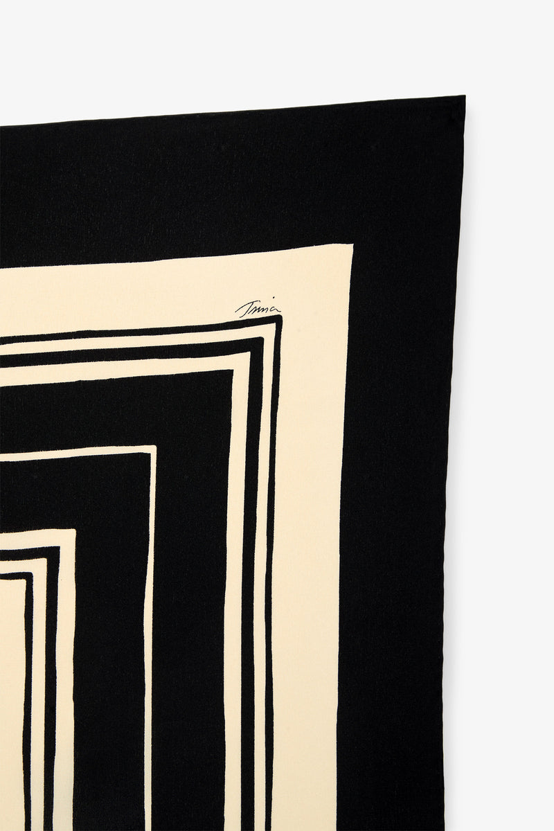 A black and cream Scala Silk Scarf featuring bold, irregular rectangular shapes arranged in a striking geometric pattern, with a handwritten signature near the top edge of the fabric.