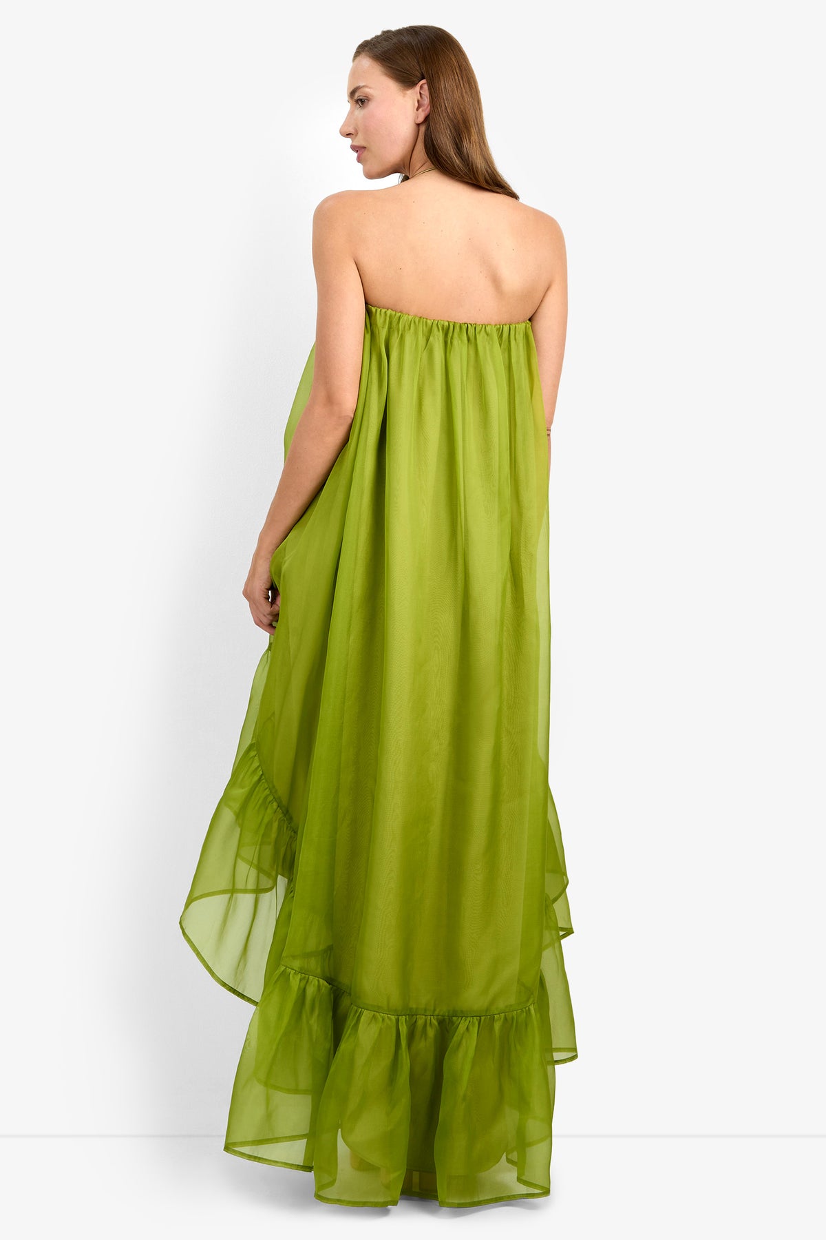 A woman with straight brown hair stands facing away against a plain white background, wearing the ARIAH DRESS—a strapless, long lime-green dress featuring a ruffled hem.