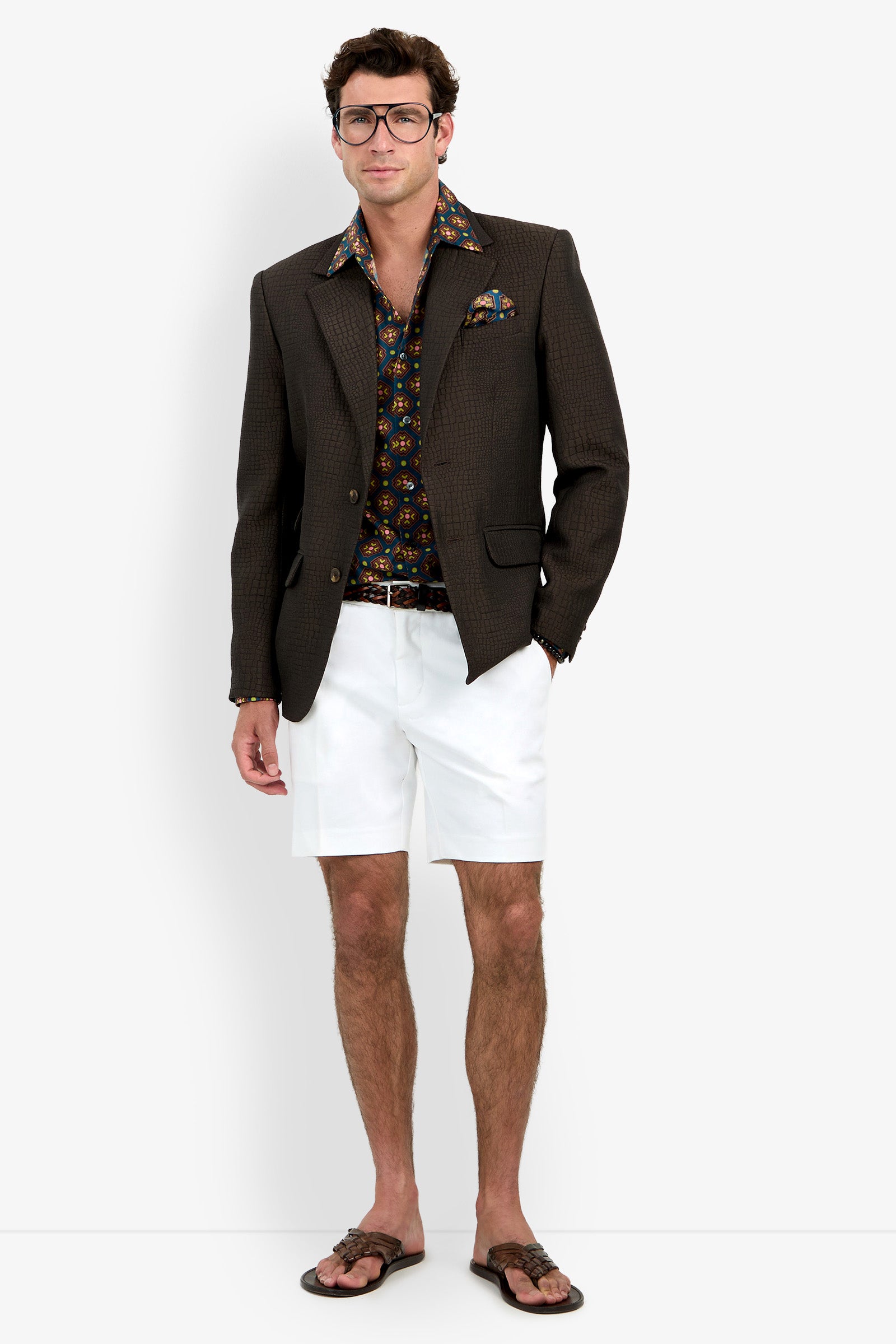 A man wearing the Dohney Blazer, a patterned shirt, white shorts, brown sandals, and glasses stands against a plain white background.