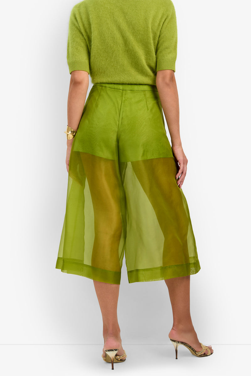 A person shown from the back wearing a light green short-sleeve sweater, sheer green Siena Pant wide-leg culottes, a gold bracelet, and snakeskin-patterned high-heeled sandals.