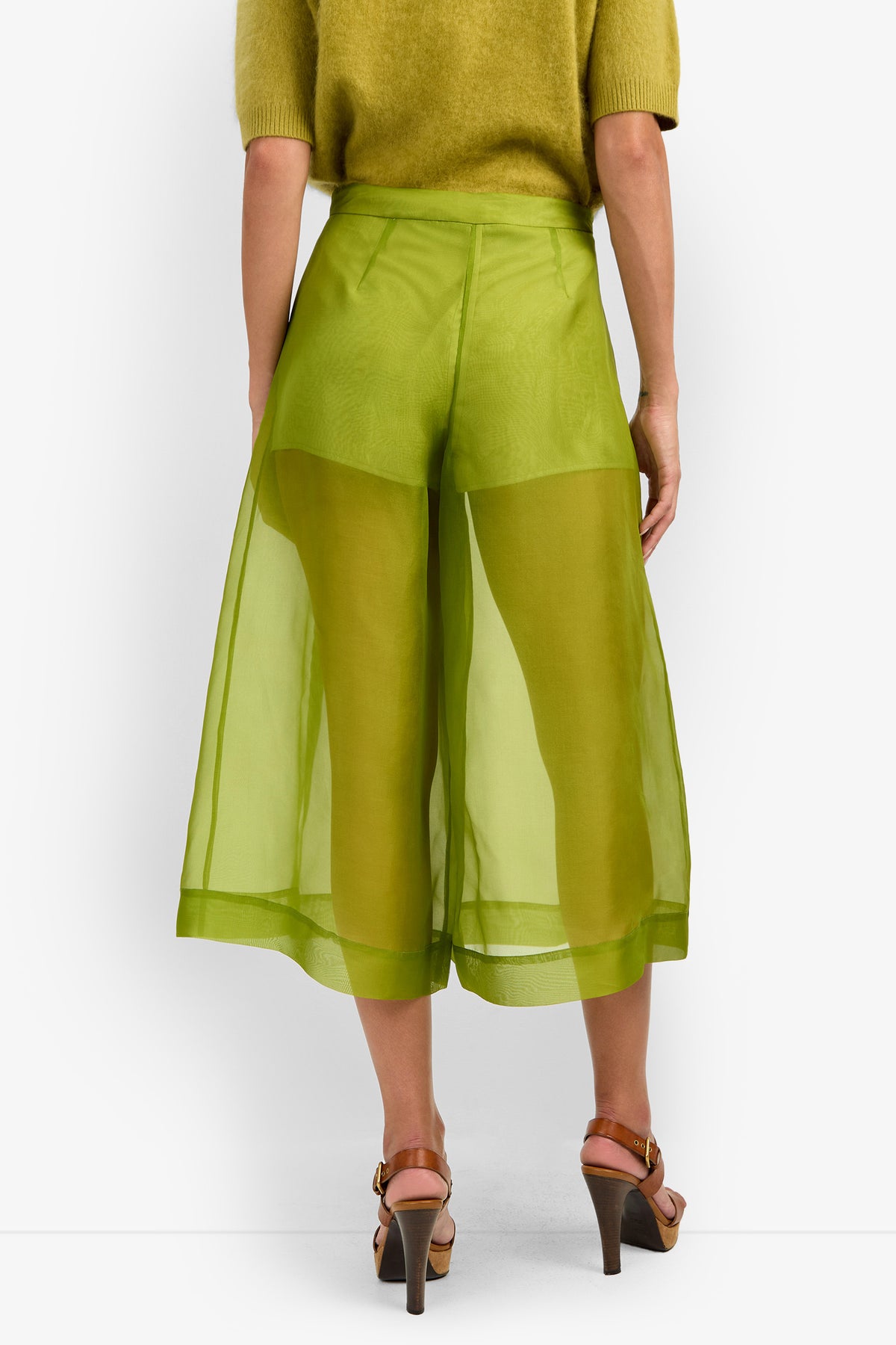 A person shown from the back is wearing the SIENA PANT in sheer, bright green with wide-leg culotte styling and visible shorts underneath, paired with a matching green top and brown heeled sandals.