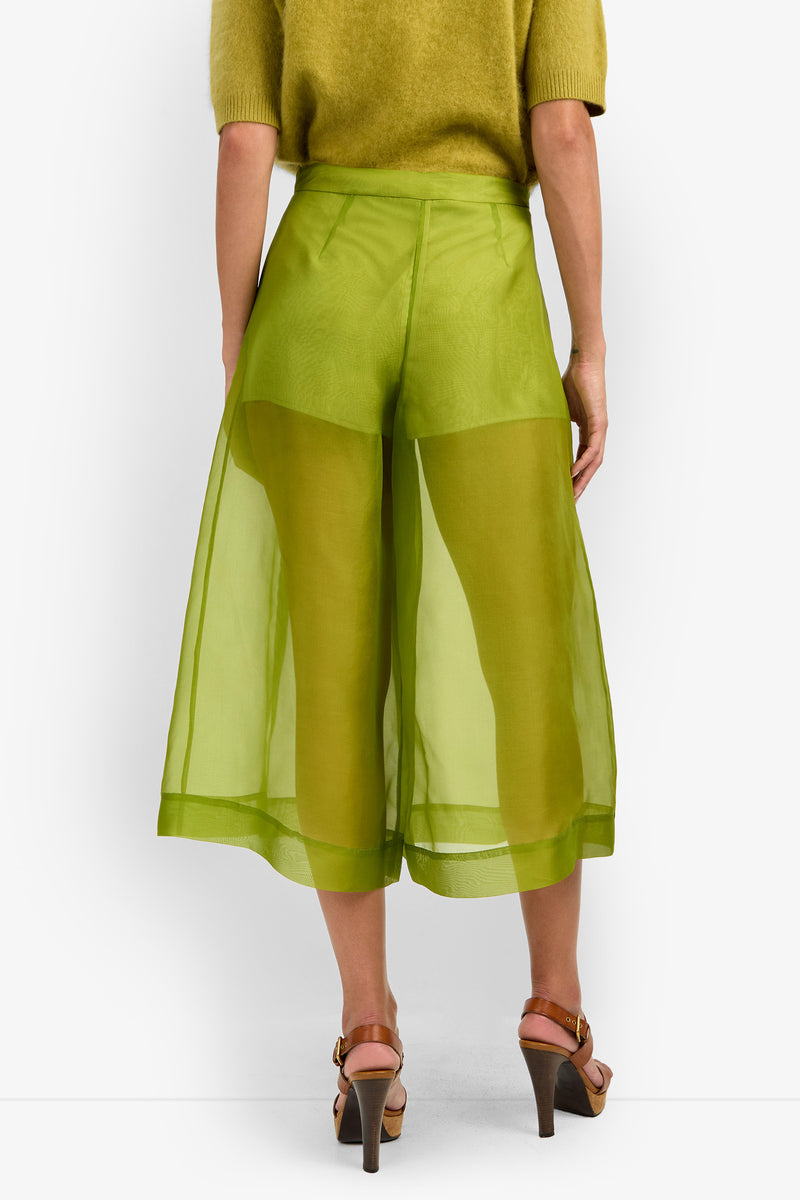 A person shown from the back is wearing the SIENA PANT in sheer, bright green with wide-leg culotte styling and visible shorts underneath, paired with a matching green top and brown heeled sandals.