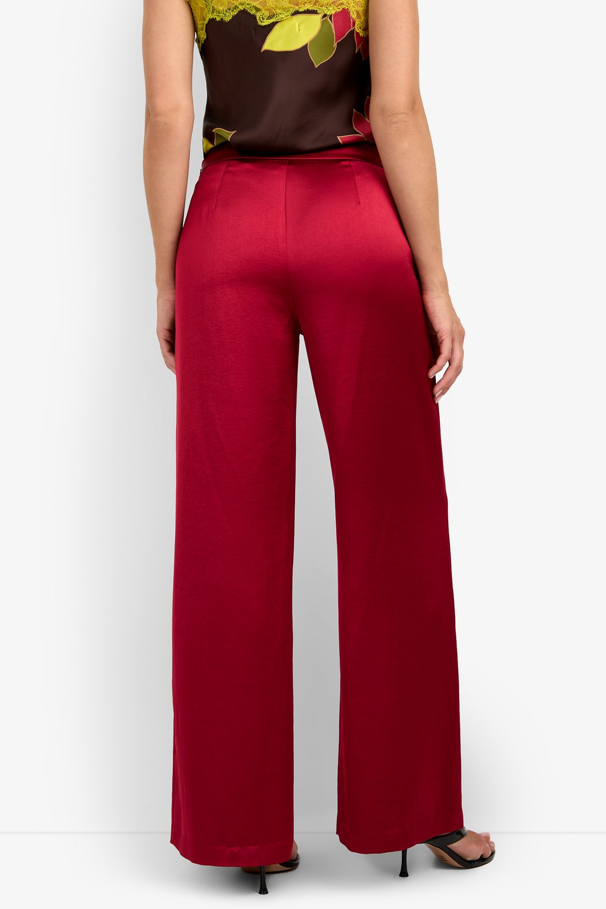 A person is standing with their back to the camera, wearing the INES PANT in a wide-leg red style, paired with a dark floral top and black heeled sandals against a plain background.