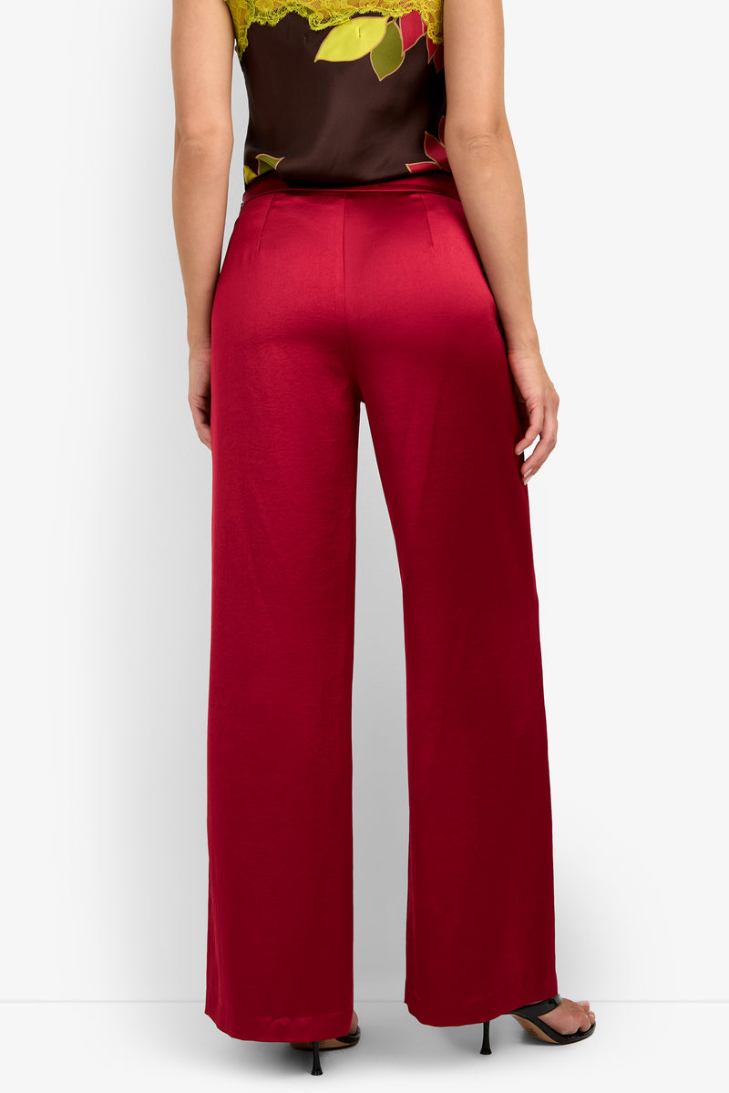 A person is standing with their back to the camera, wearing the INES PANT in a wide-leg red style, paired with a dark floral top and black heeled sandals against a plain background.