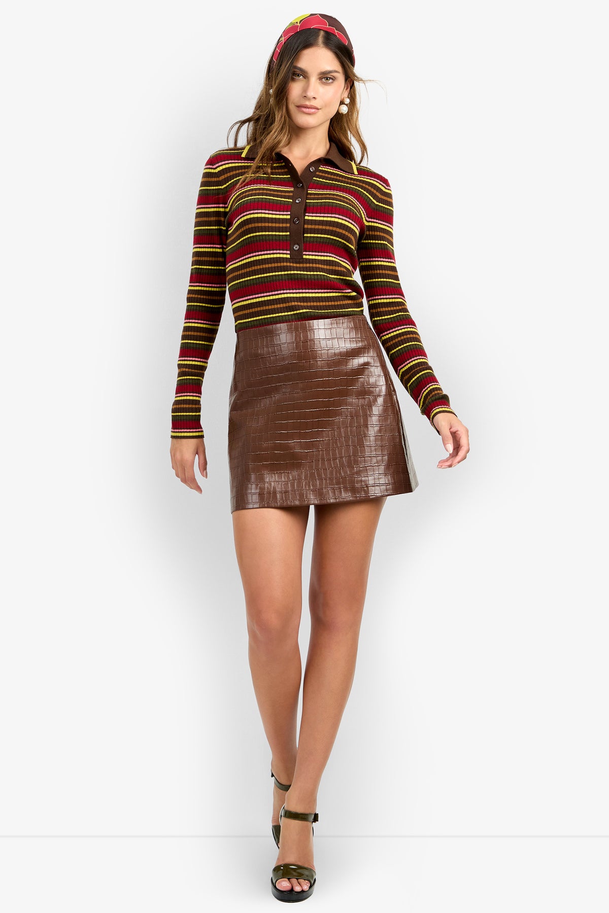 A woman wearing the Rico Skirt, paired with a striped long-sleeve shirt, green heels, and a red headband, stands against a white background.