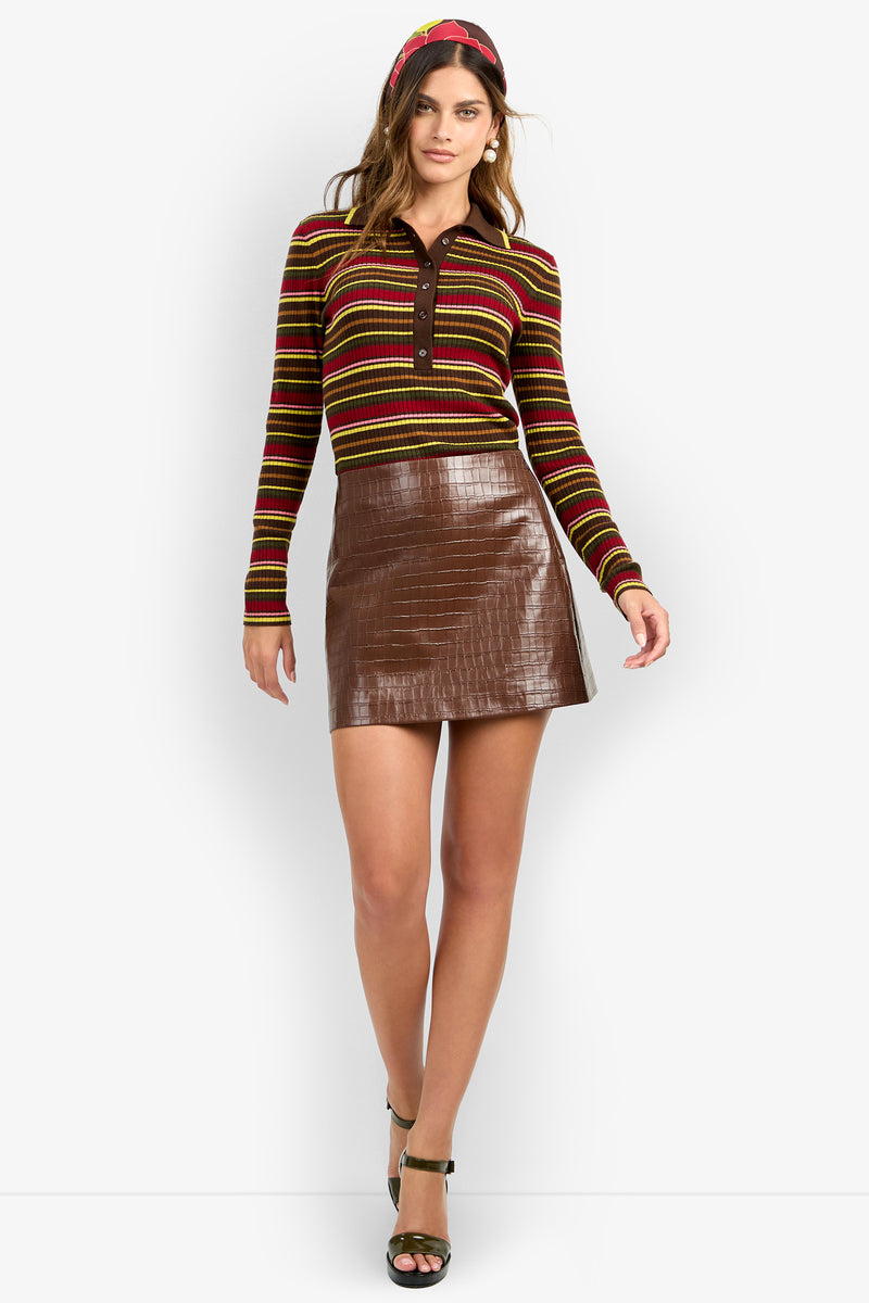 A woman wearing the Rico Skirt, paired with a striped long-sleeve shirt, green heels, and a red headband, stands against a white background.