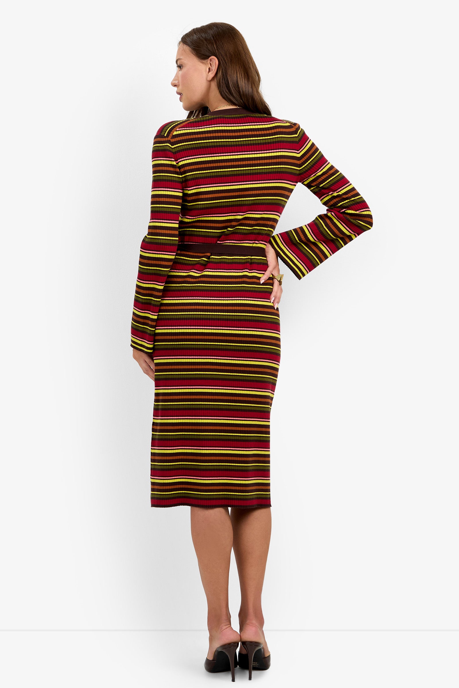 A woman stands in heels, facing away, wearing the Mercer Sweater Dress—a long-sleeve, knee-length style featuring horizontal yellow, green, pink, and maroon stripes with a cutout detail at the waist.