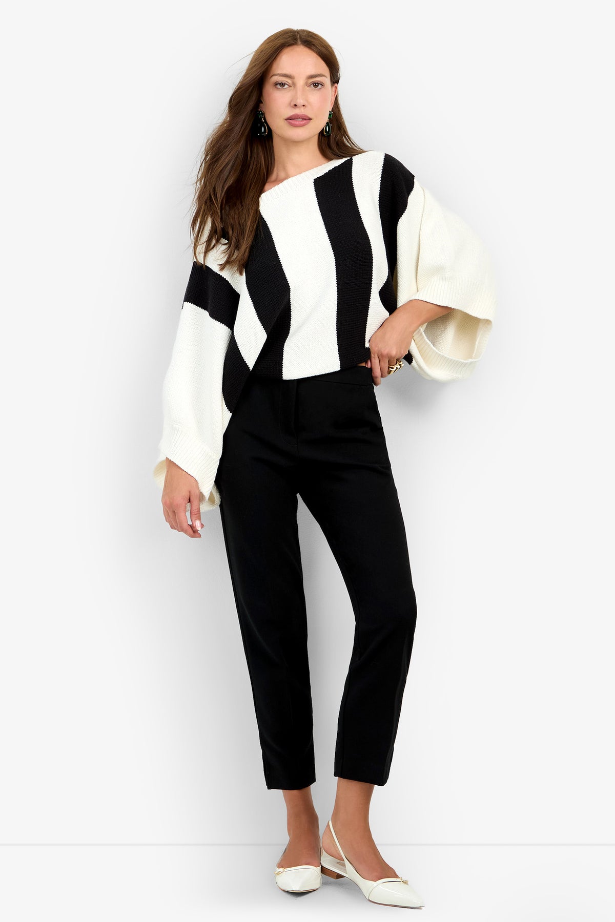 A woman wears a Horizon Sweater with wide black and white vertical stripes, paired with black trousers and white pointed-toe flats.