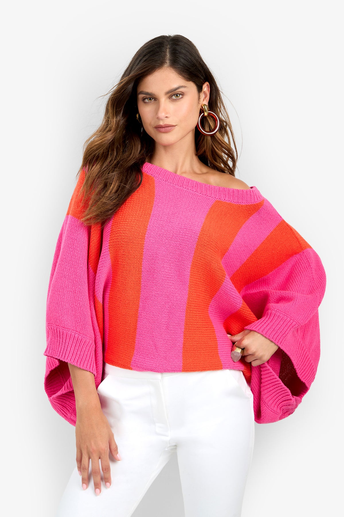 A model wearing a Horizon Sweater featuring an oversized, boat-neck design with wide vertical pink and orange stripes and three-quarter length dolman sleeves.