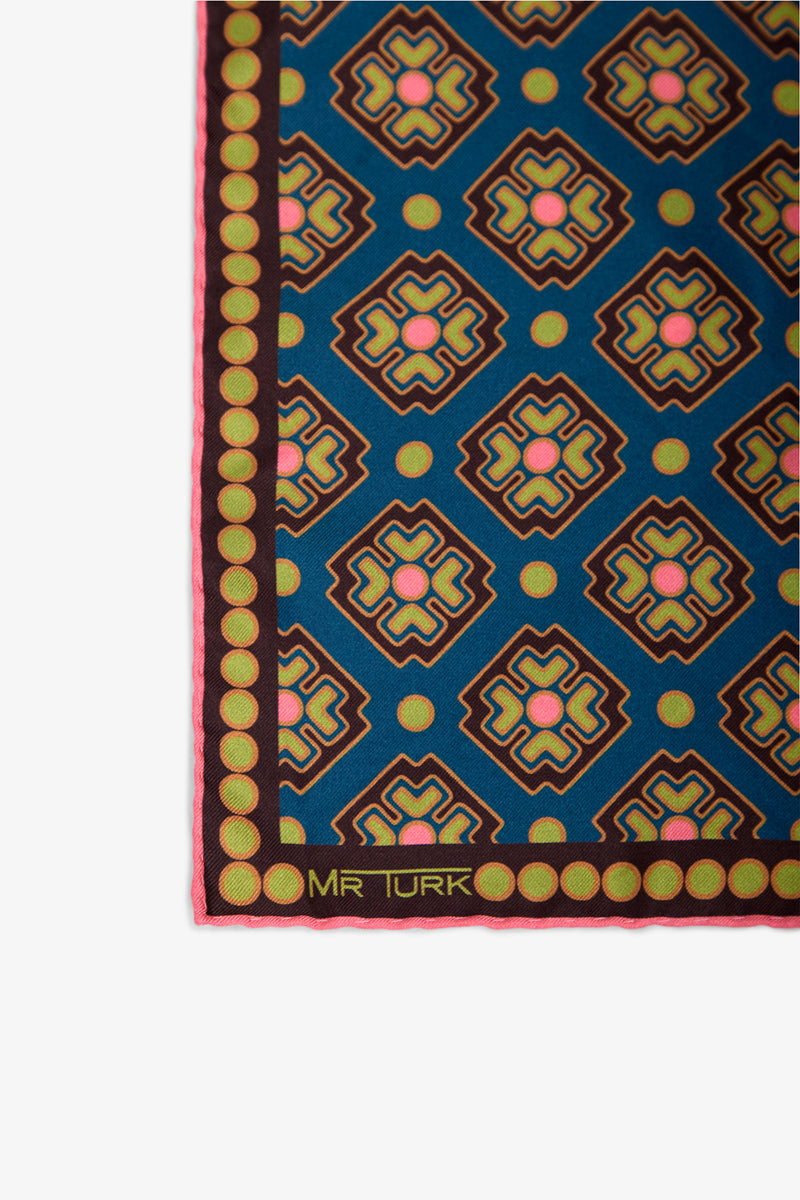 Colorful geometric patterned Pocket Square featuring blue, gold, pink, and brown shapes. The border is brown with green circles, and “MR TURK” is printed in the lower left corner. Only part of the Pocket Square is shown.