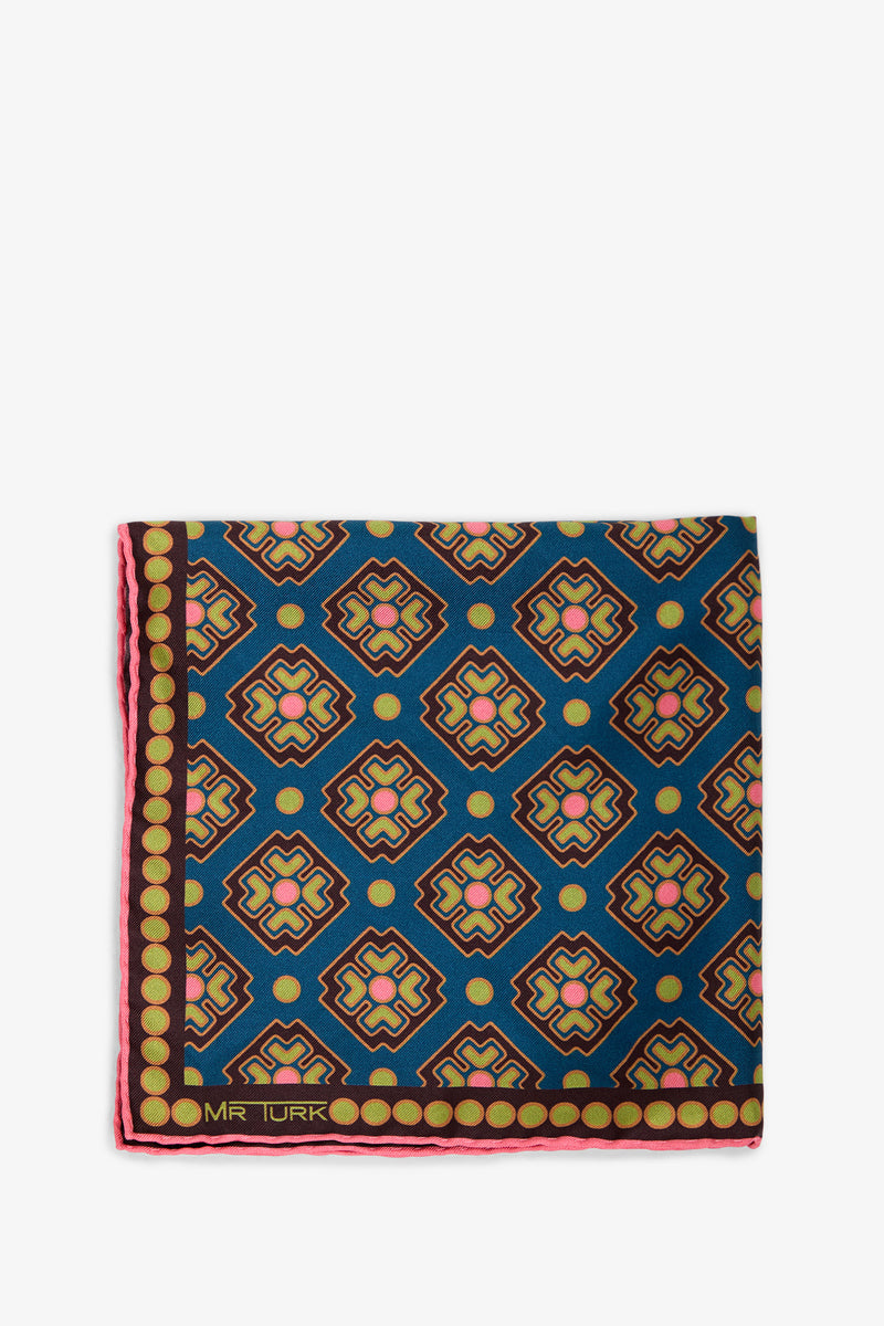 A folded Pocket Square featuring a geometric pattern in blue, pink, yellow, and black, accented by a border of yellow dots with “MR TURK” printed in the corner.