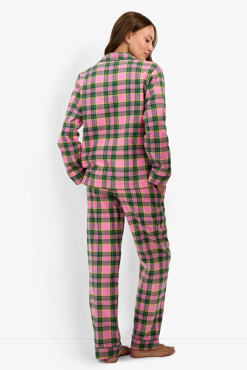 A person stands barefoot, facing away and wearing the Tartan Long Sleeve PJ Set in a pink, green, and white plaid pattern. The background is plain white.