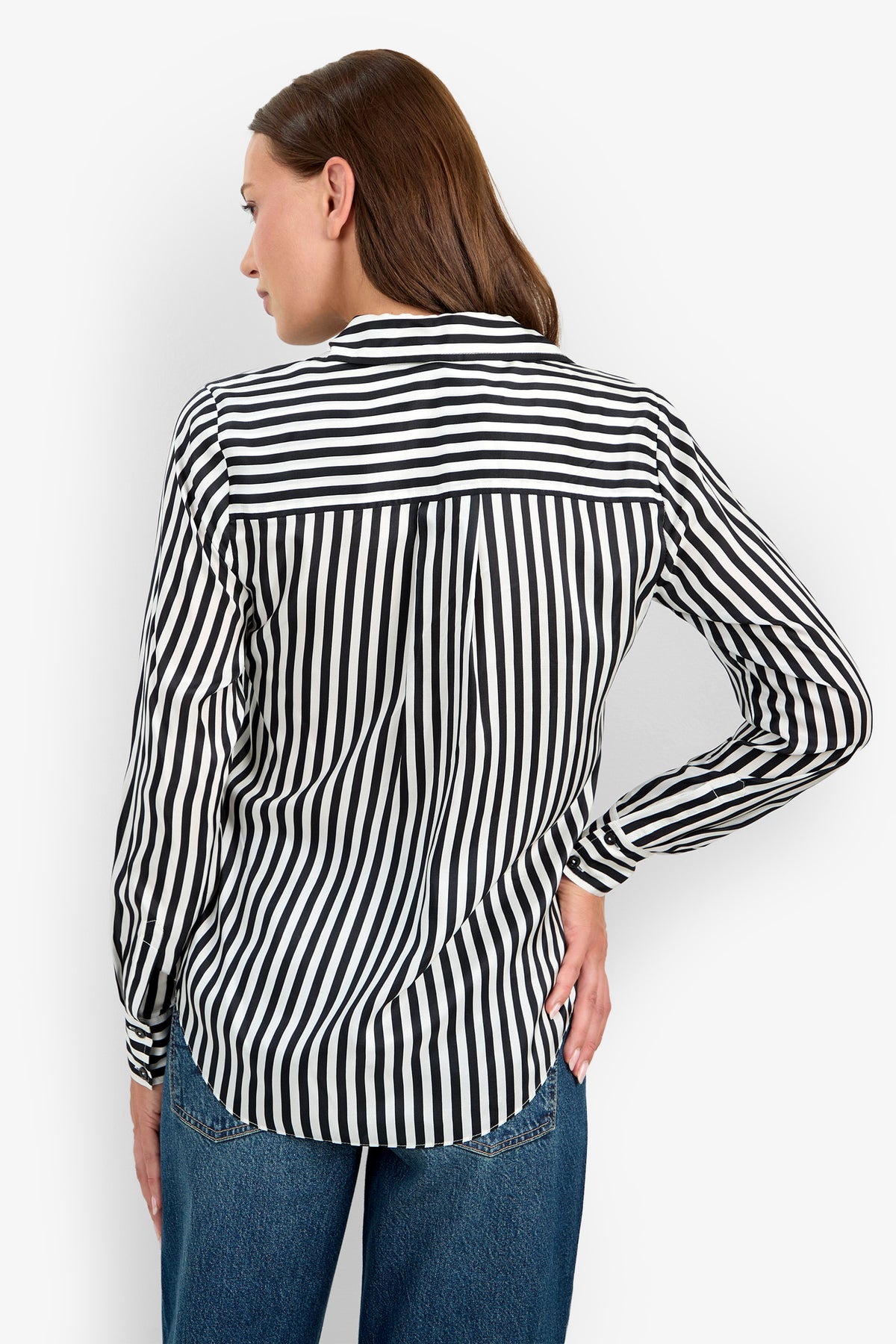 A woman with brown hair is pictured from the back, standing with one hand on her hip, wearing blue jeans and the Rouge Top—a black and white vertically striped long-sleeve shirt.