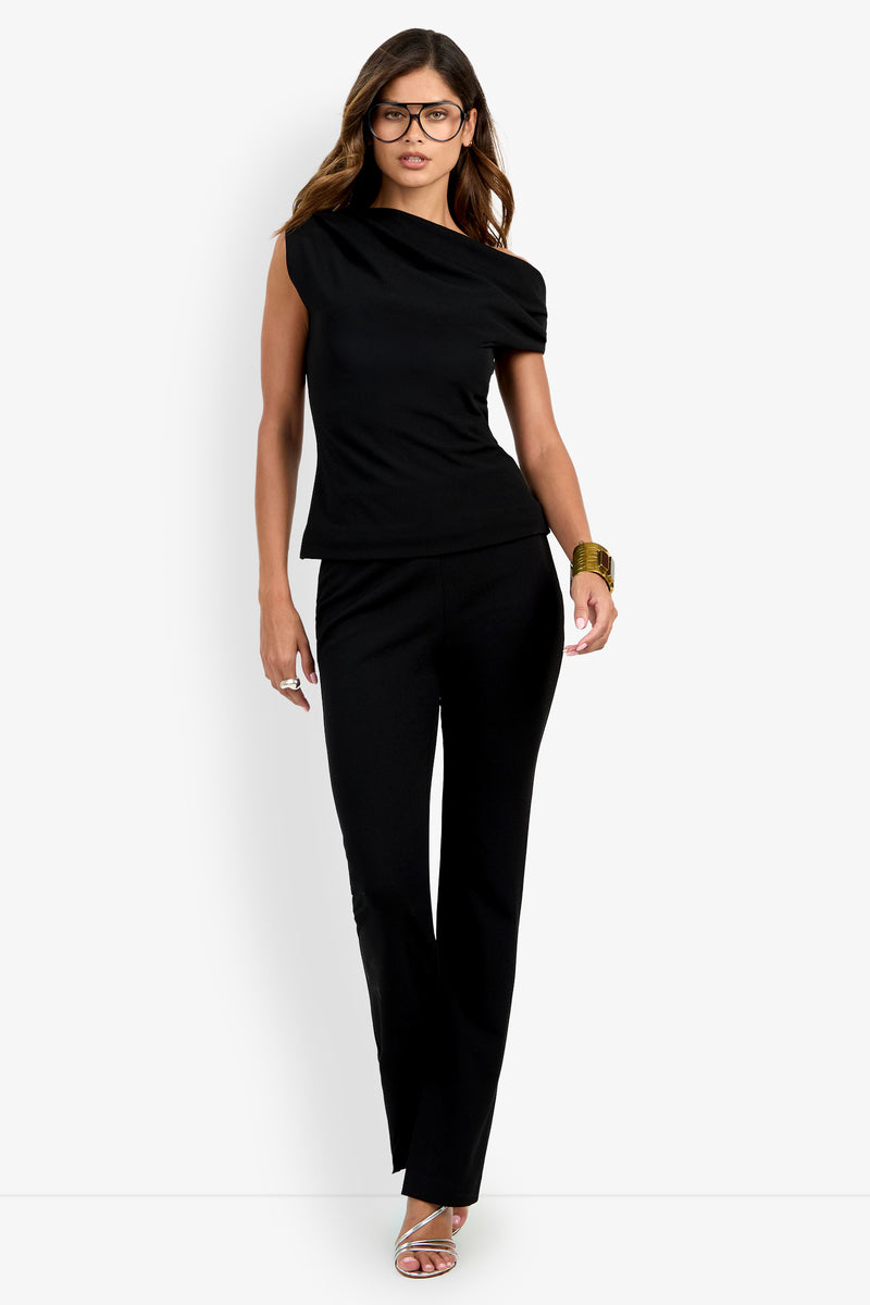 A woman wearing the Roza Top in black, paired with pants, silver heels, a brown bangle, and glasses, stands against a white background.