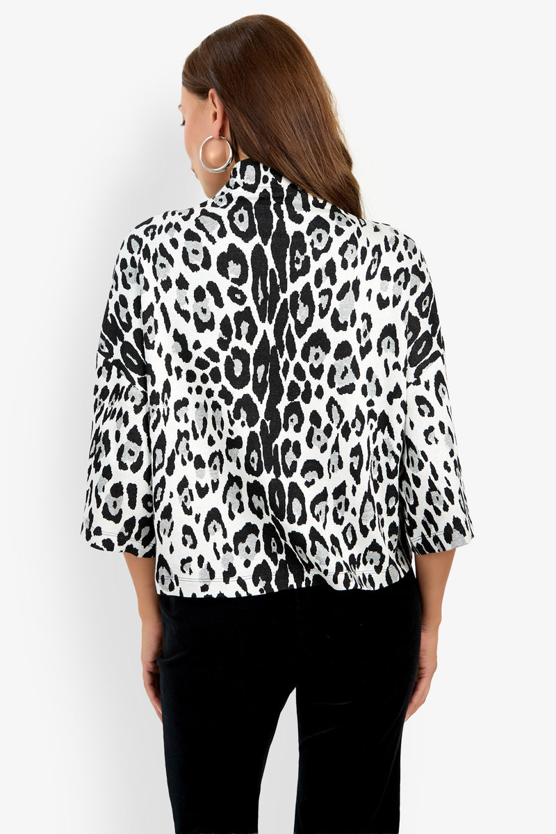 Woman with long brown hair, wearing large hoop earrings and the Sidony Top—a black and white animal print jacket with wide sleeves—paired with black pants, shown from the back against a plain white background.