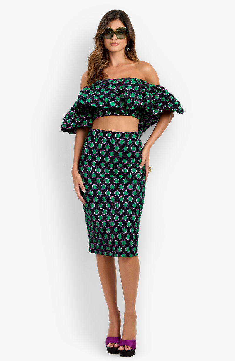 A woman wearing sunglasses, an off-shoulder ruffled crop top, and the Soniah Skirt—a matching high-waisted midi skirt with a green and purple pattern—stands against a plain white background.