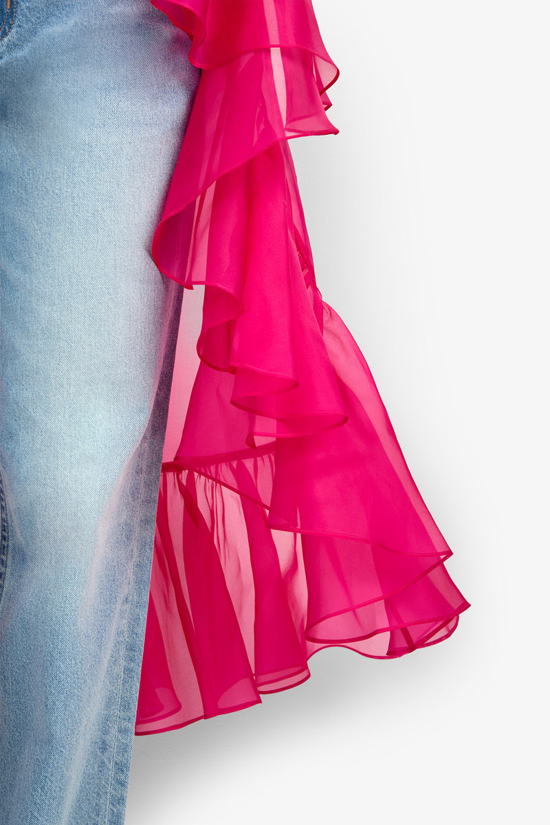 Close-up of the Aries Jacket in light blue denim, featuring a sheer, ruffled hot pink fabric draped over one side, set against a white background.