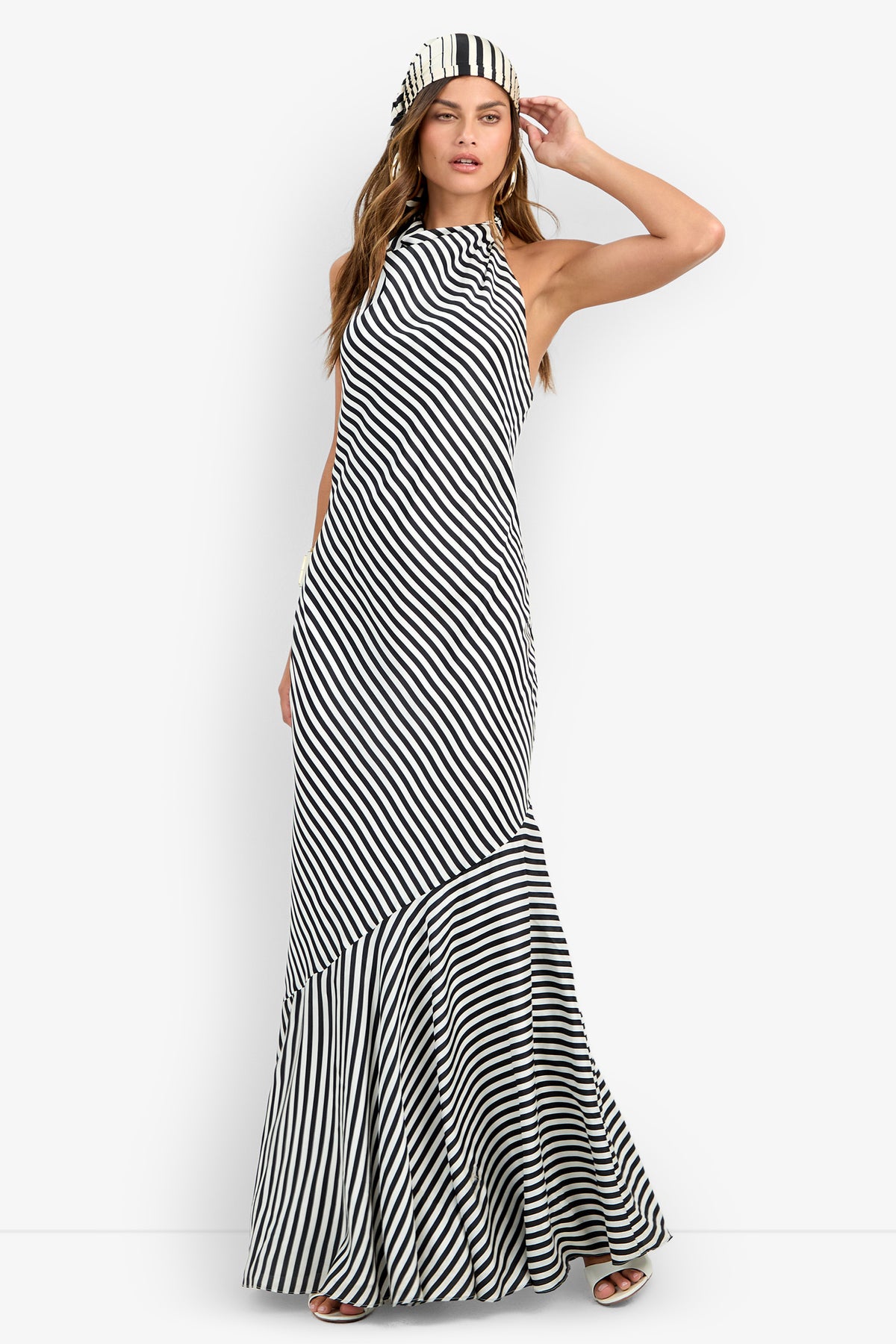 A woman models the Lady Dress, a long, sleeveless black and white diagonal striped dress with a high neckline and matching striped headband, posing with one hand on her head against a plain white background.