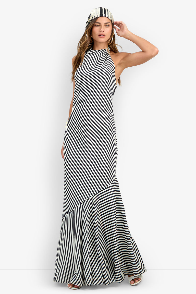 A woman models the Lady Dress, a long, sleeveless black and white diagonal striped dress with a high neckline and matching striped headband, posing with one hand on her head against a plain white background.