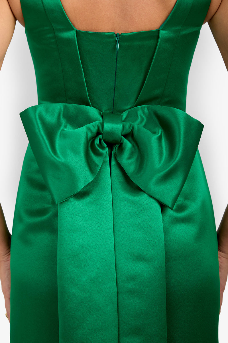 A close-up of the back of the Philia Dress in green satin, showcasing a large, elegant bow at the waist and a visible zipper above the bow.