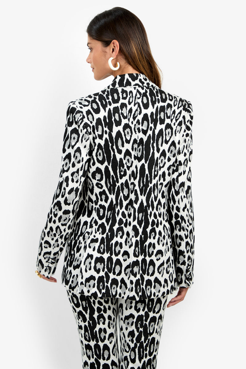 A person with long brown hair wears the Bacino Jacket— a black and white leopard print blazer—along with matching pants, facing away from the camera against a plain white background.