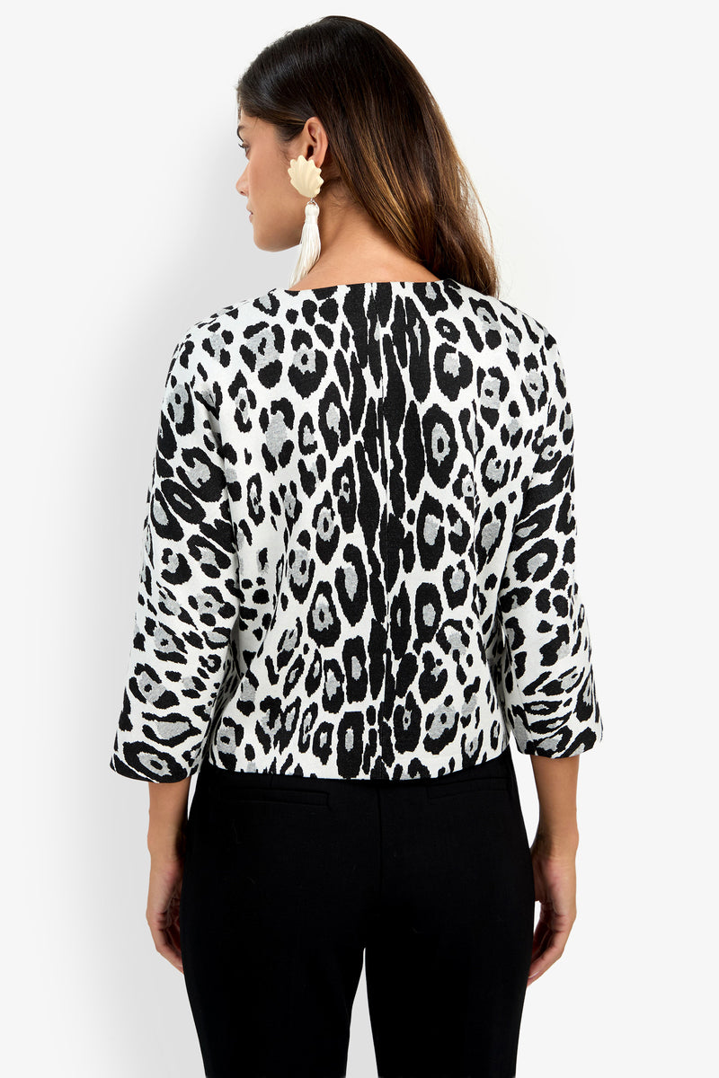 Woman facing away, wearing the Critique Jacket in a black-and-white animal print with three-quarter sleeves, paired with black pants and large white earrings.