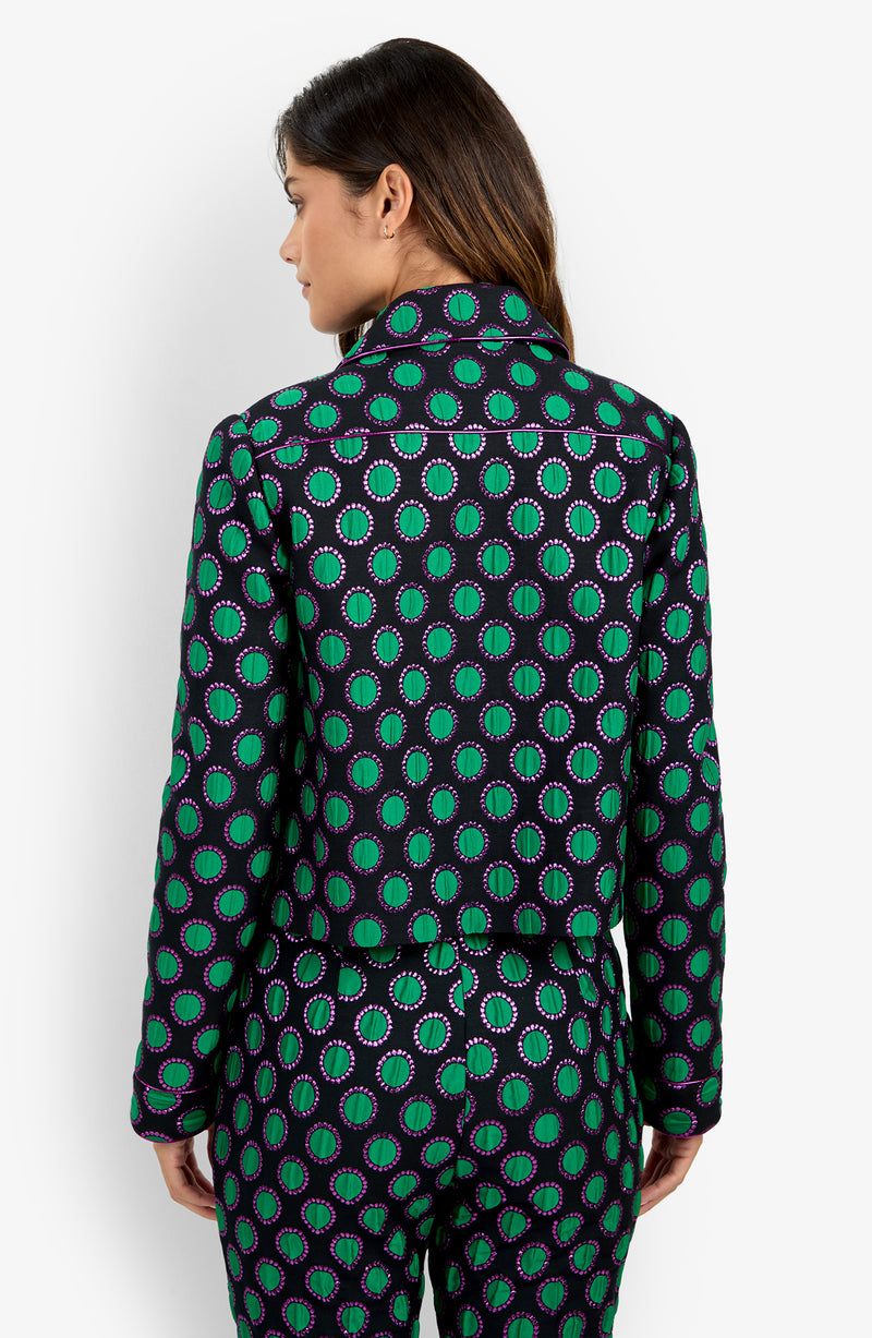 A person with long brown hair, facing away from the camera, wears the Allex Jacket as part of a matching set featuring a green, purple, and black circular geometric pattern.