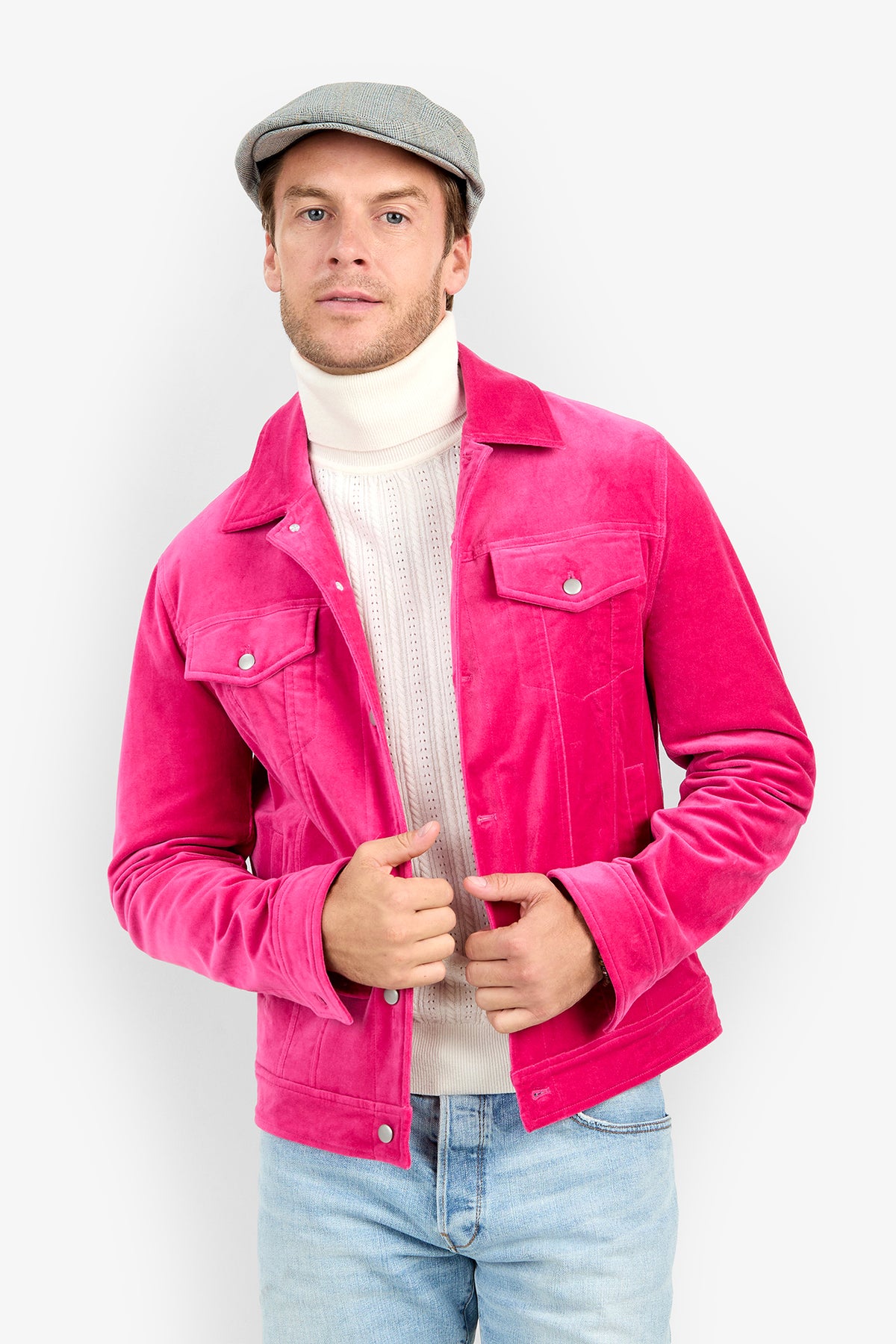 A man wearing a bright pink Angelino Trucker Jacket over a white turtleneck sweater, light blue jeans, and a grey flat cap.