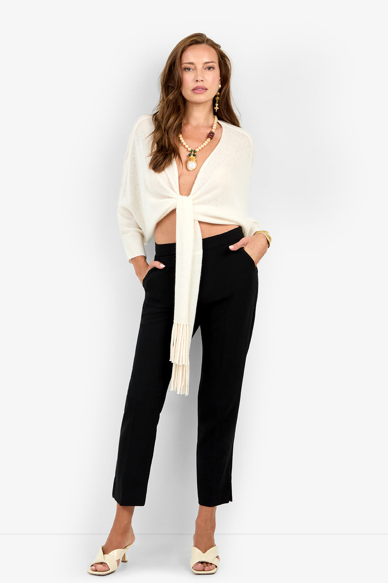 A woman wears black ankle-length ARNO PANT trousers, a cream-colored tie-front sweater, and cream mules.