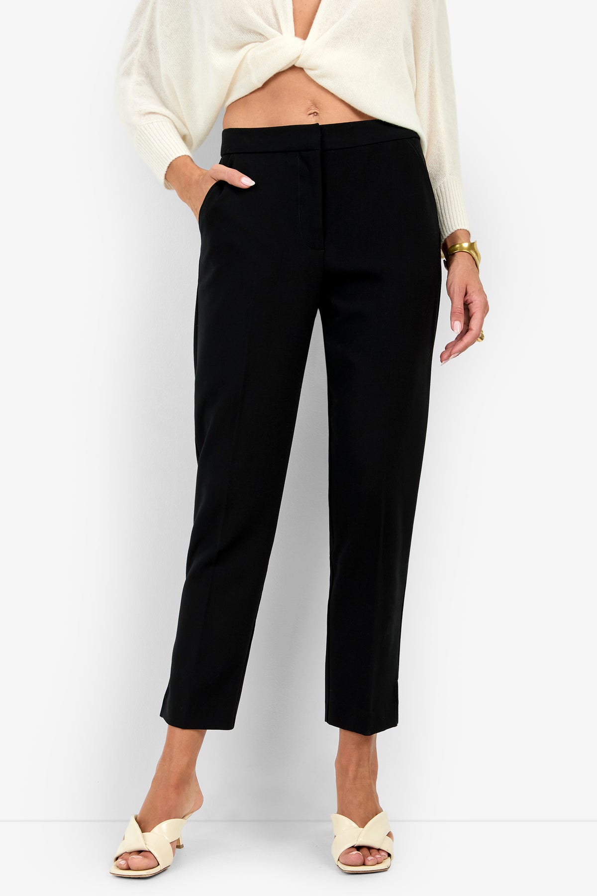 Black high-waisted ARNO PANT cropped trousers with side pockets, worn with a white long-sleeved top and cream slide sandals.