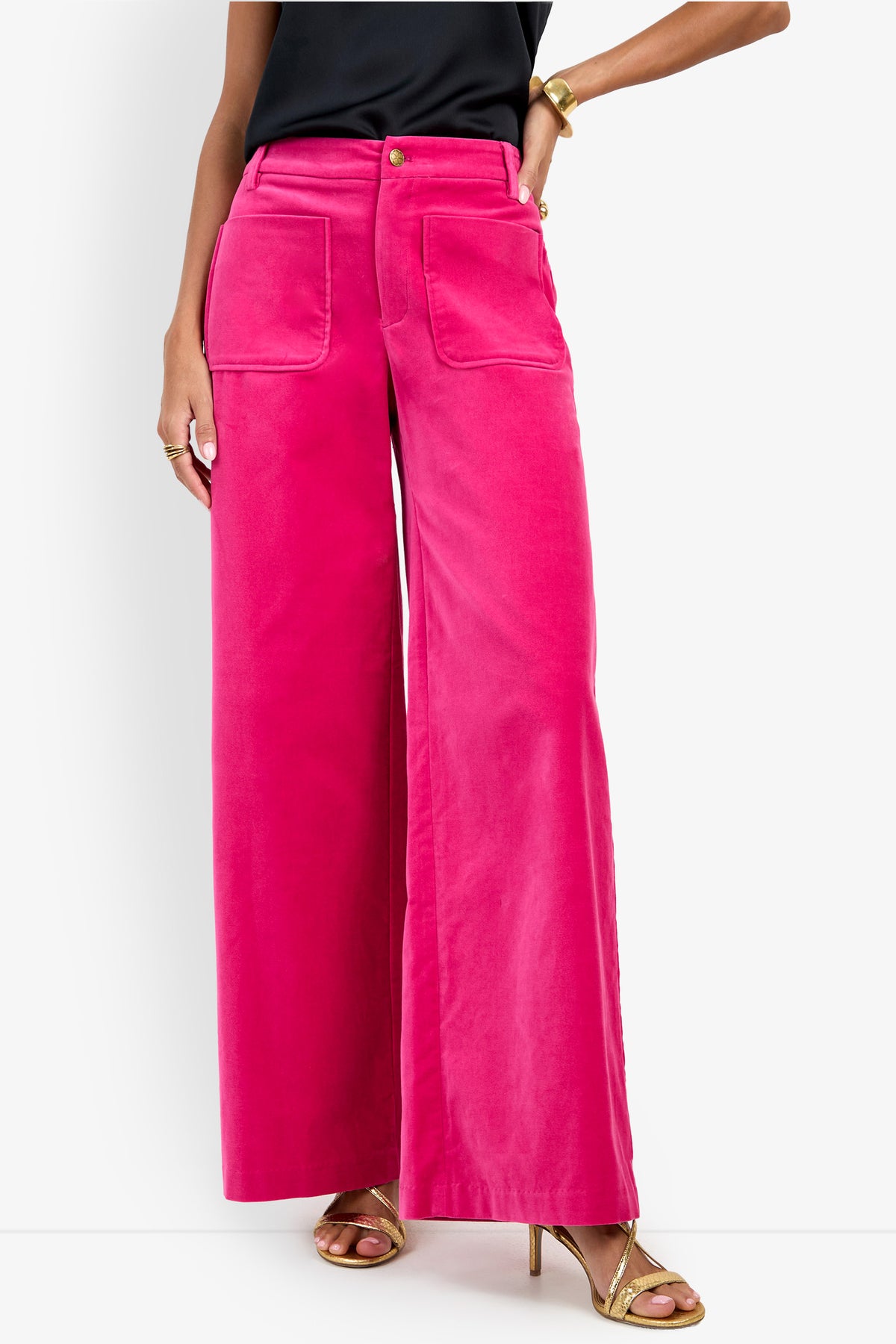 A person wearing the Talamone Pant—bright pink wide-leg pants with front pockets—paired with a black top, gold high-heeled sandals, and gold jewelry, stands against a white background.