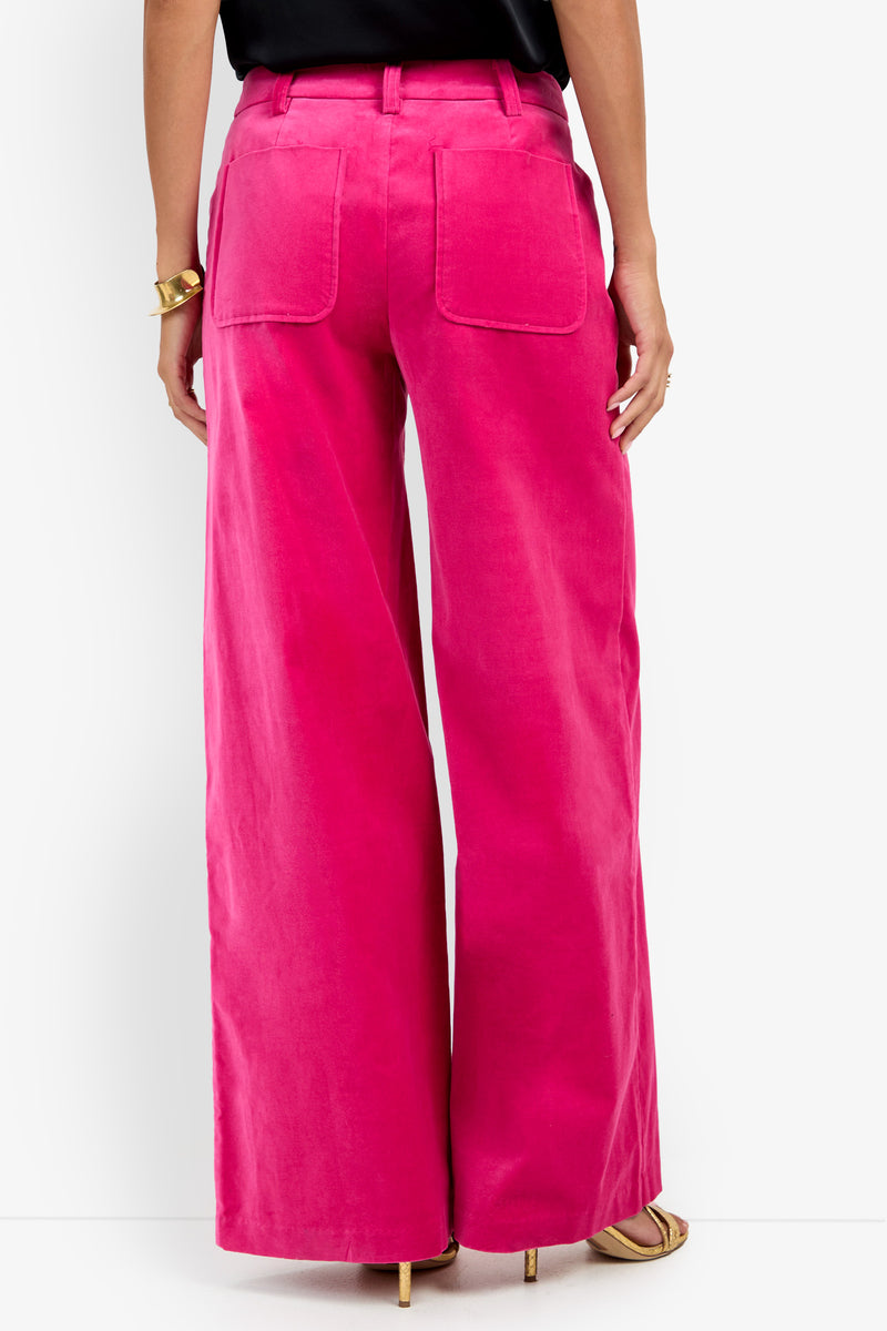 A person seen from the back wearing Talamone Pant in bright pink with back pockets, paired with a black top, gold bracelet, and beige heeled sandals.