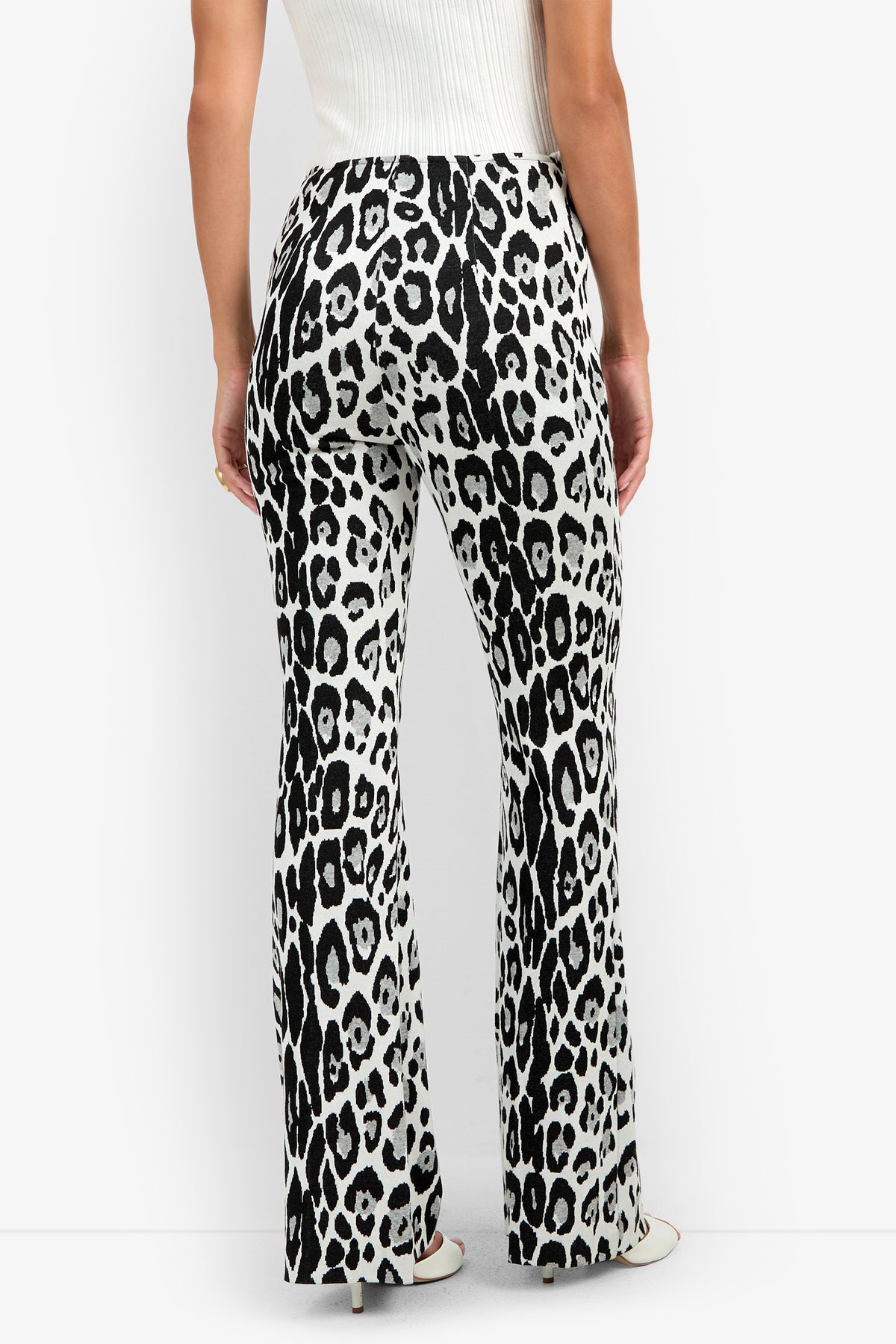 A person wearing the Jacoba Pant, featuring a high-waisted, black and white leopard print flare design, paired with a white sleeveless top and shown from the back against a plain white background.