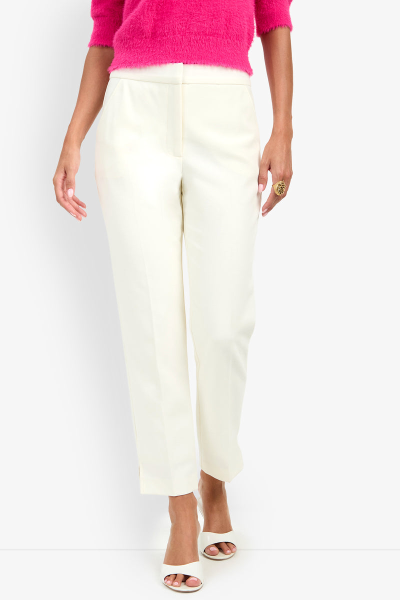 A person wearing the Arno Pant in white, paired with a fuzzy bright pink top, white open-toed heels, and a large ring on their right hand, stands against a plain background.