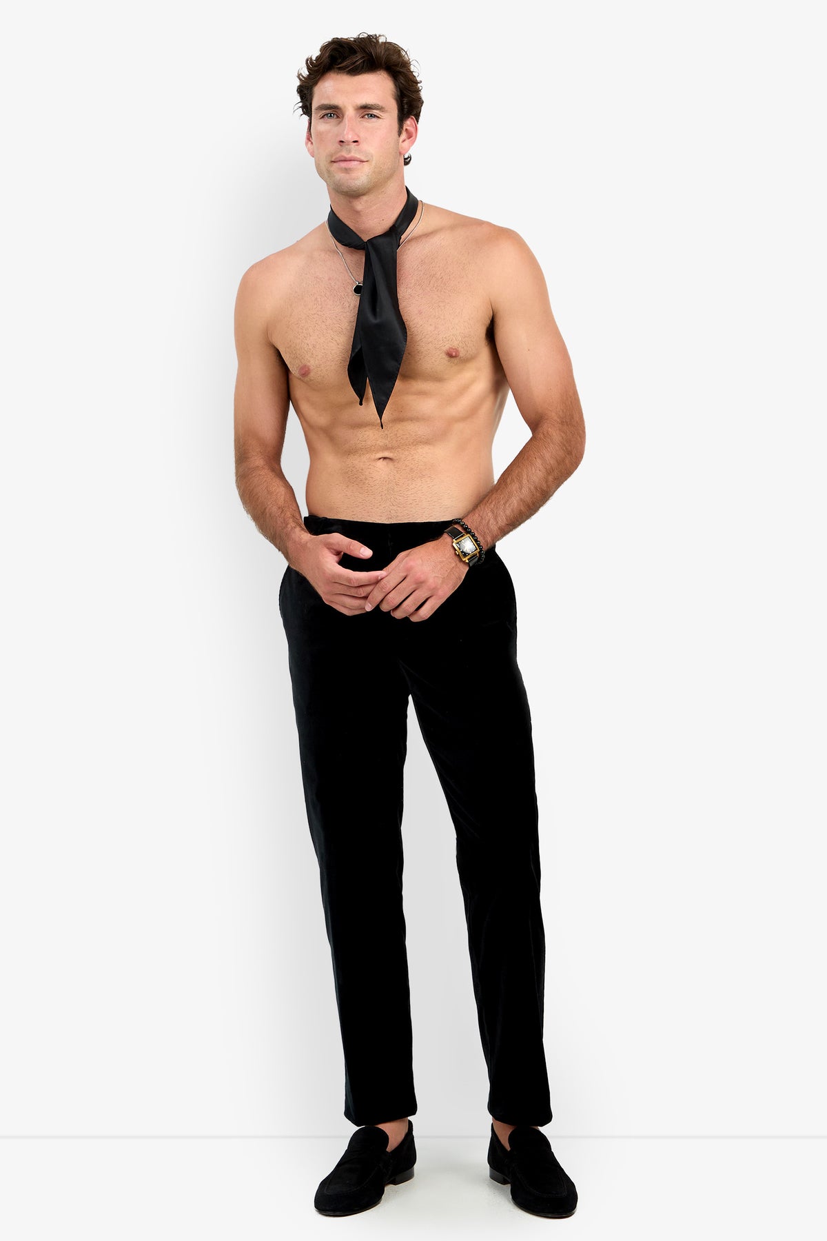 A shirtless man wearing the Clyde Slim Trouser, black loafers, a wristwatch, and a loose black necktie stands against a plain white background.
