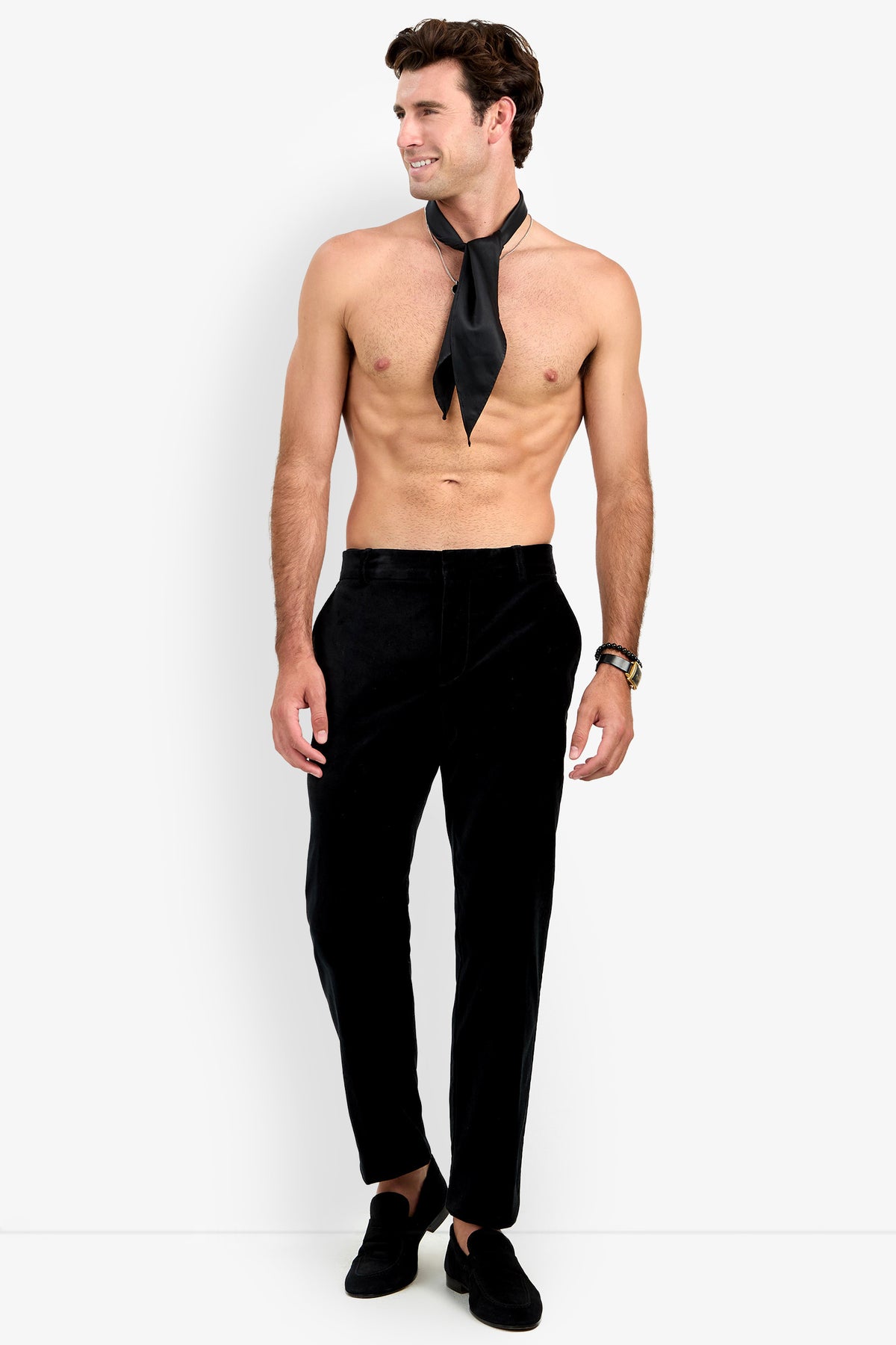 A shirtless man wearing the Clyde Slim Trouser, black shoes, and a loosely tied black necktie stands against a white background, looking to the side and smiling.