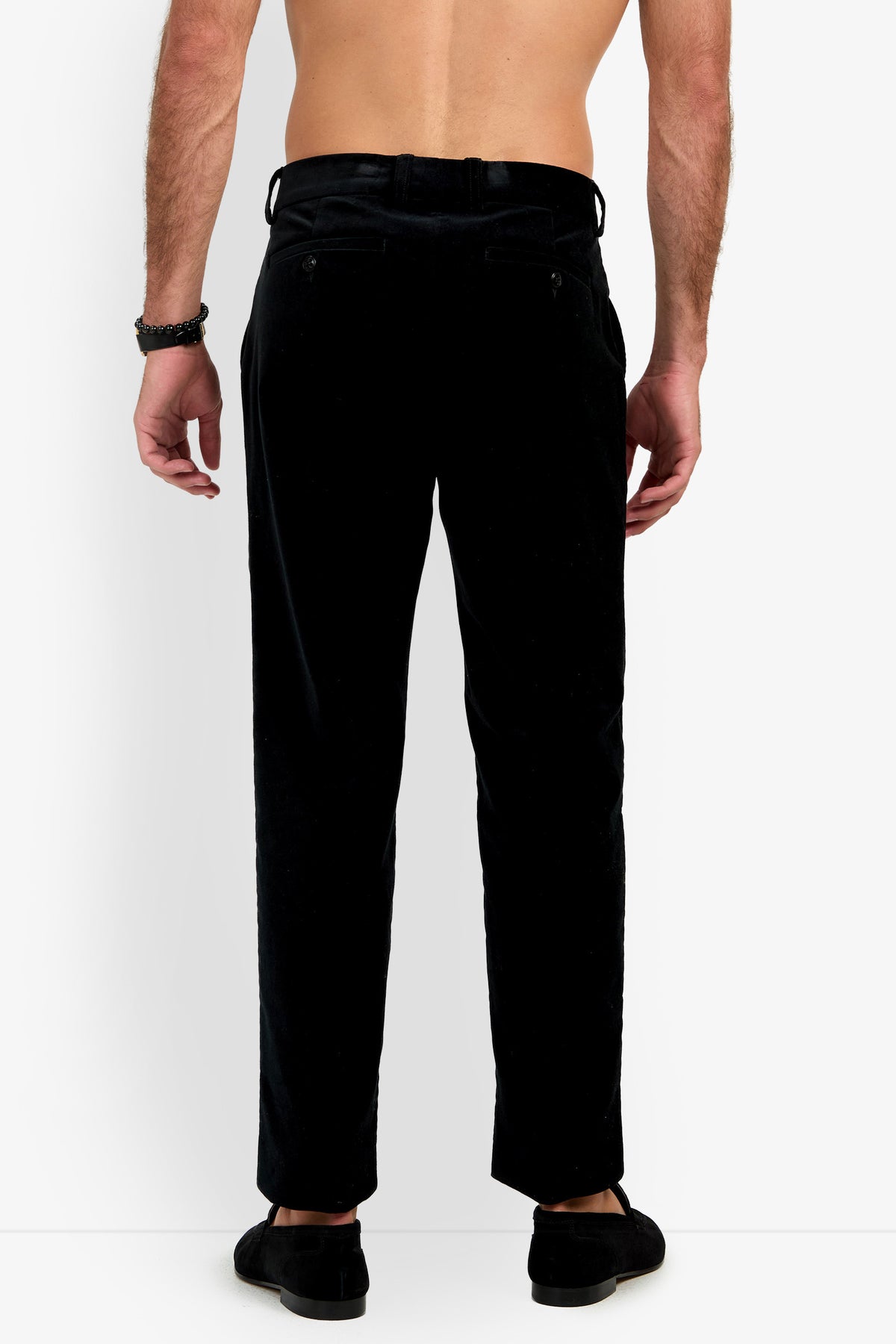 A man stands facing away from the camera, shirtless, wearing the Clyde Slim Trouser in black and black shoes. Both arms are relaxed at his sides, and he is standing against a plain white background.