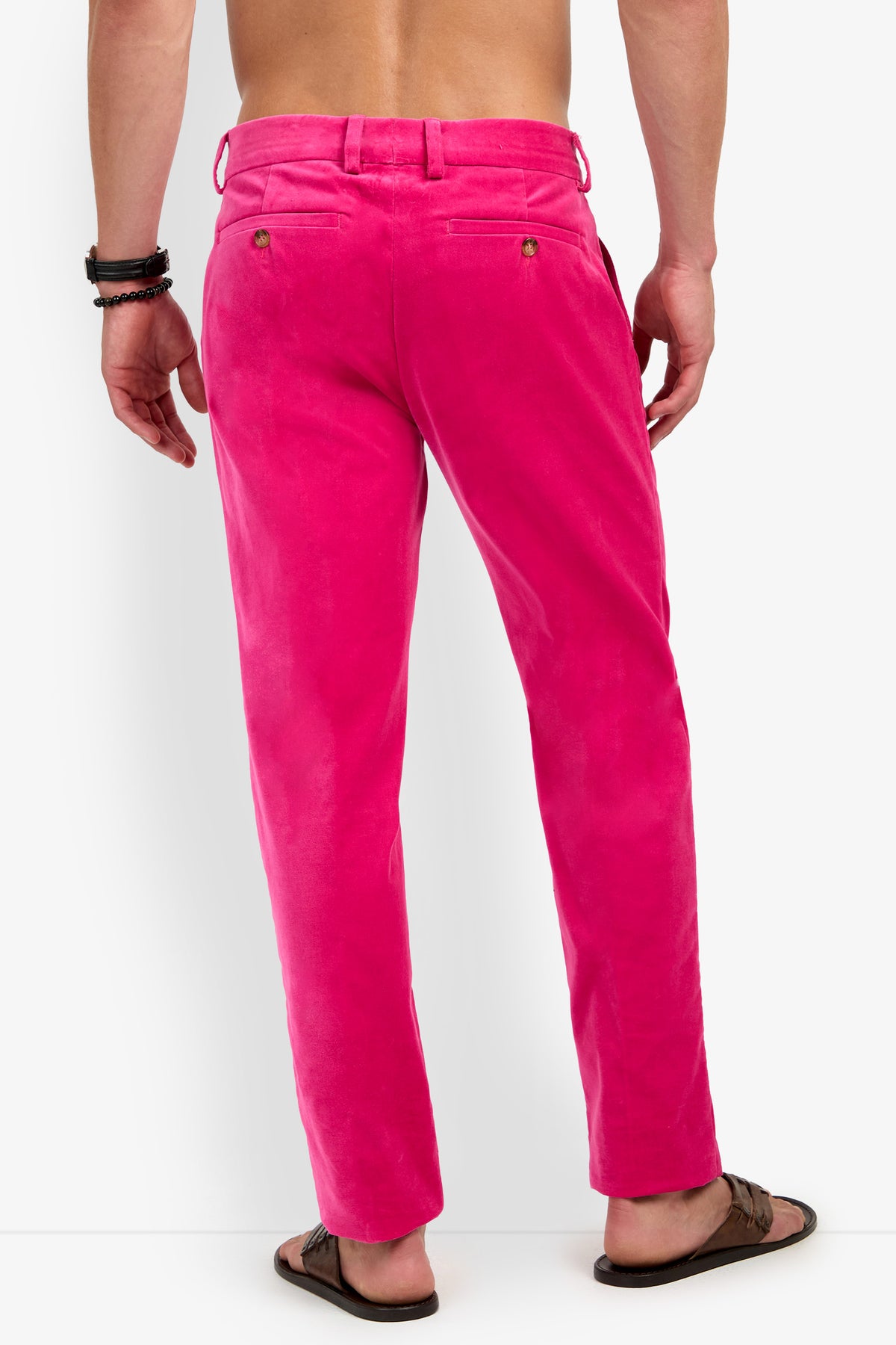 A man stands with his back to the camera, wearing bright pink Clyde Slim Trousers, paired with brown sandals and black bracelets. His upper body is bare, and the background is plain white.