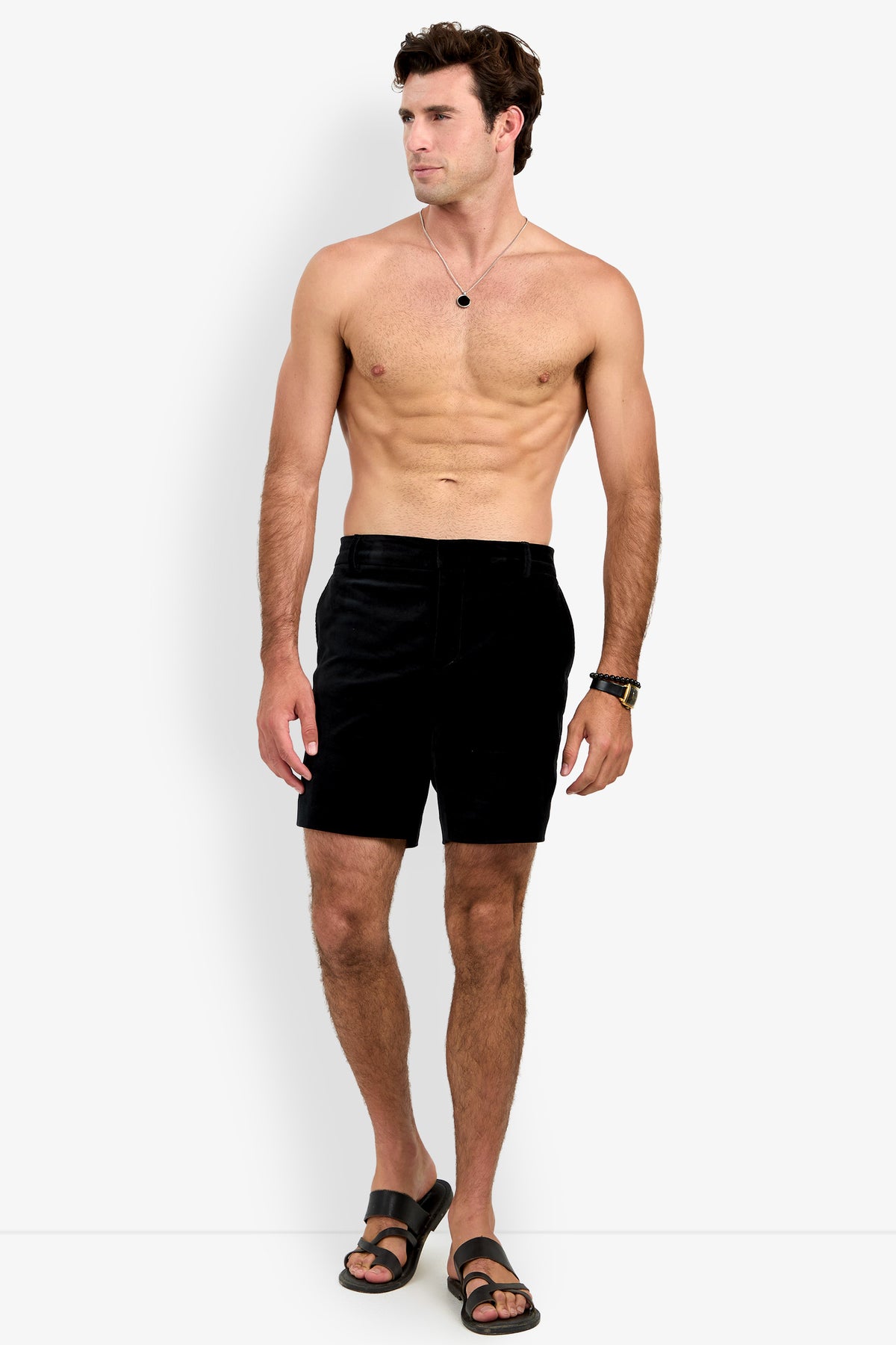 Wearing the LAWRENCE SHORT, a shirtless man stands against a white background, paired with black sandals, a necklace, and a watch, gazing slightly to his left.