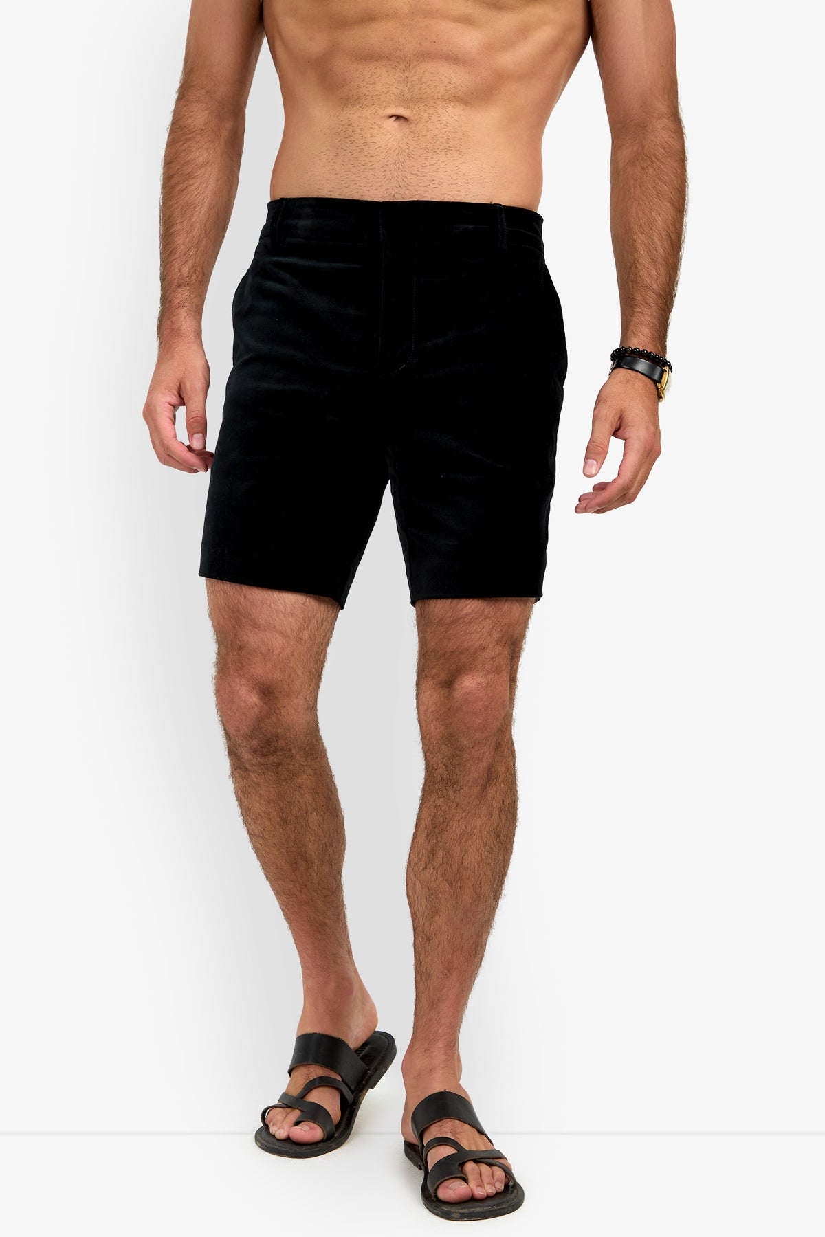A man models the LAWRENCE SHORT, paired with black sandals and a watch. His upper body is bare and his hands rest relaxed by his sides against a plain white background.