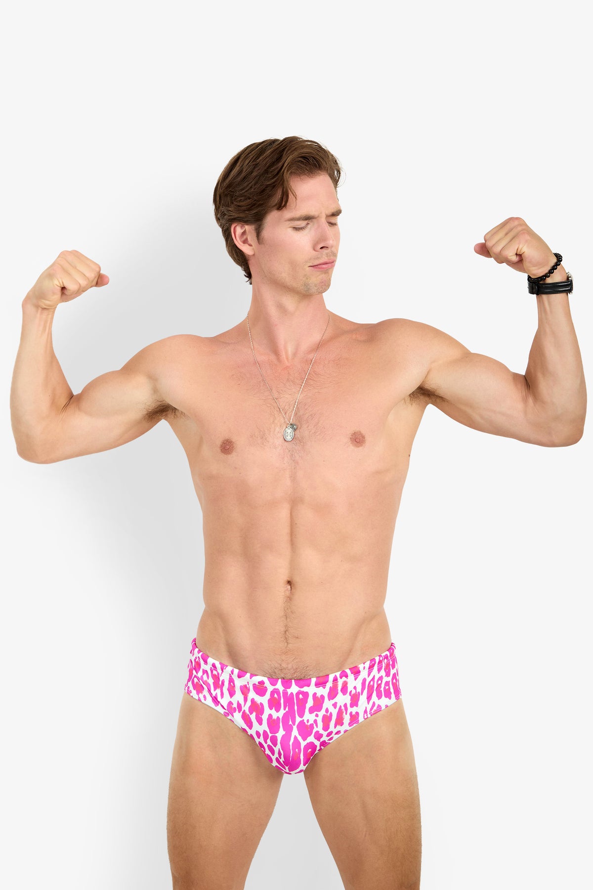 A shirtless man flexing his arms, wearing a necklace and the BONDI SWIM BRIEF in a pink-and-white animal print, stands against a plain white background.