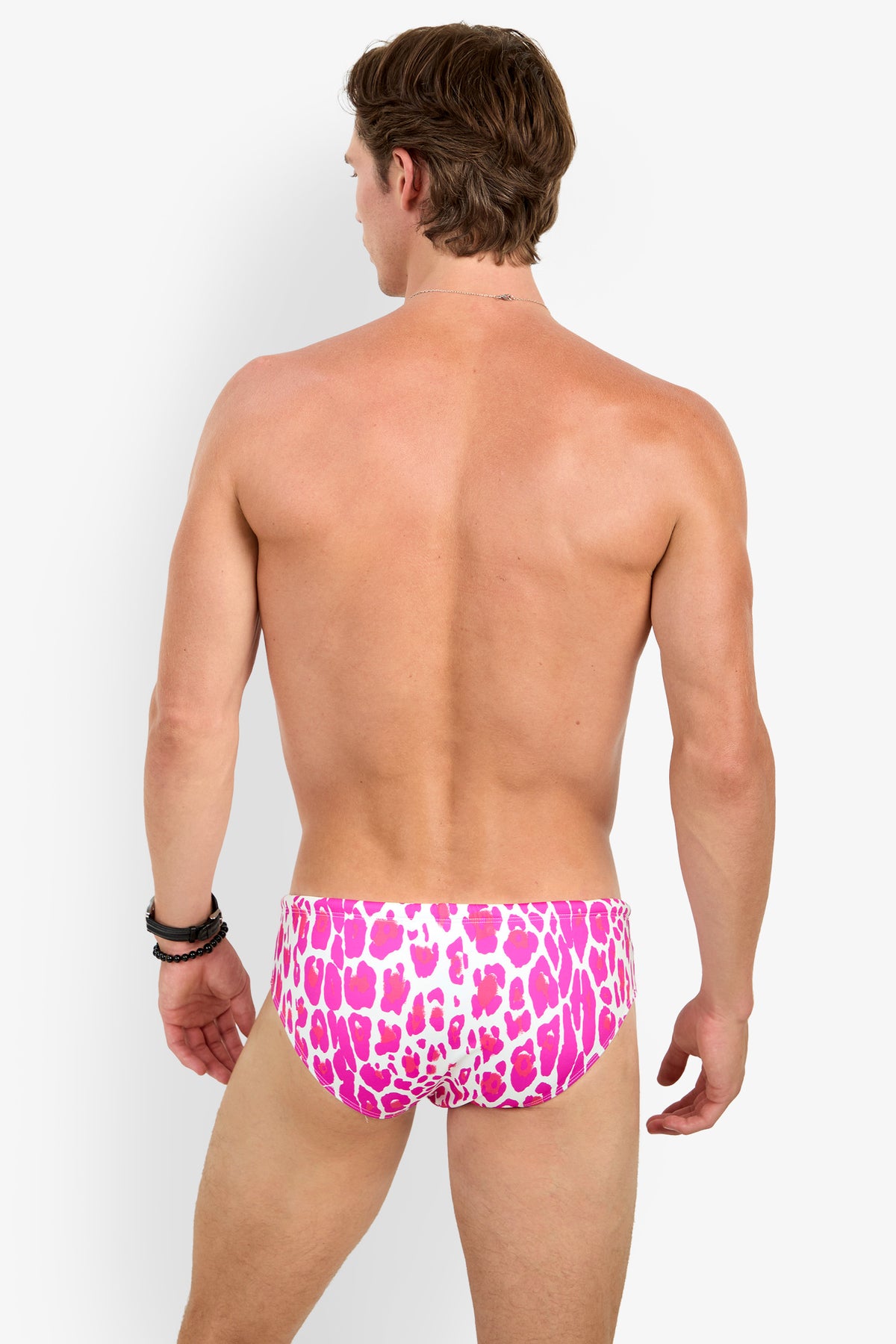 A man stands facing away, wearing the BONDI SWIM BRIEF in a pink and white animal print. He is shirtless, with one arm relaxed and the other slightly bent, set against a plain white background.