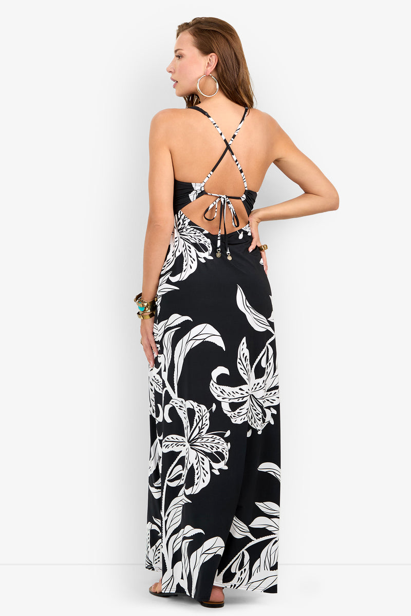 A woman seen from the back wearing a black floral GOLDEN HOUR BLOOM MAXI DRESS, featuring a tie-back bodice and thin crisscross straps.
