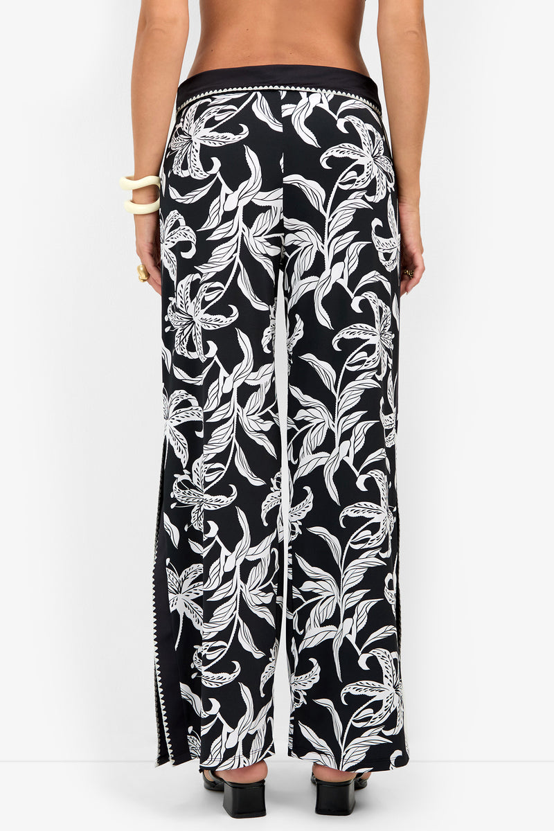 Back view of GOLDEN HOUR BLOOM SWIM PANT, featuring high-waisted, wide-leg floral swim pants in a black and white pattern with side slits.