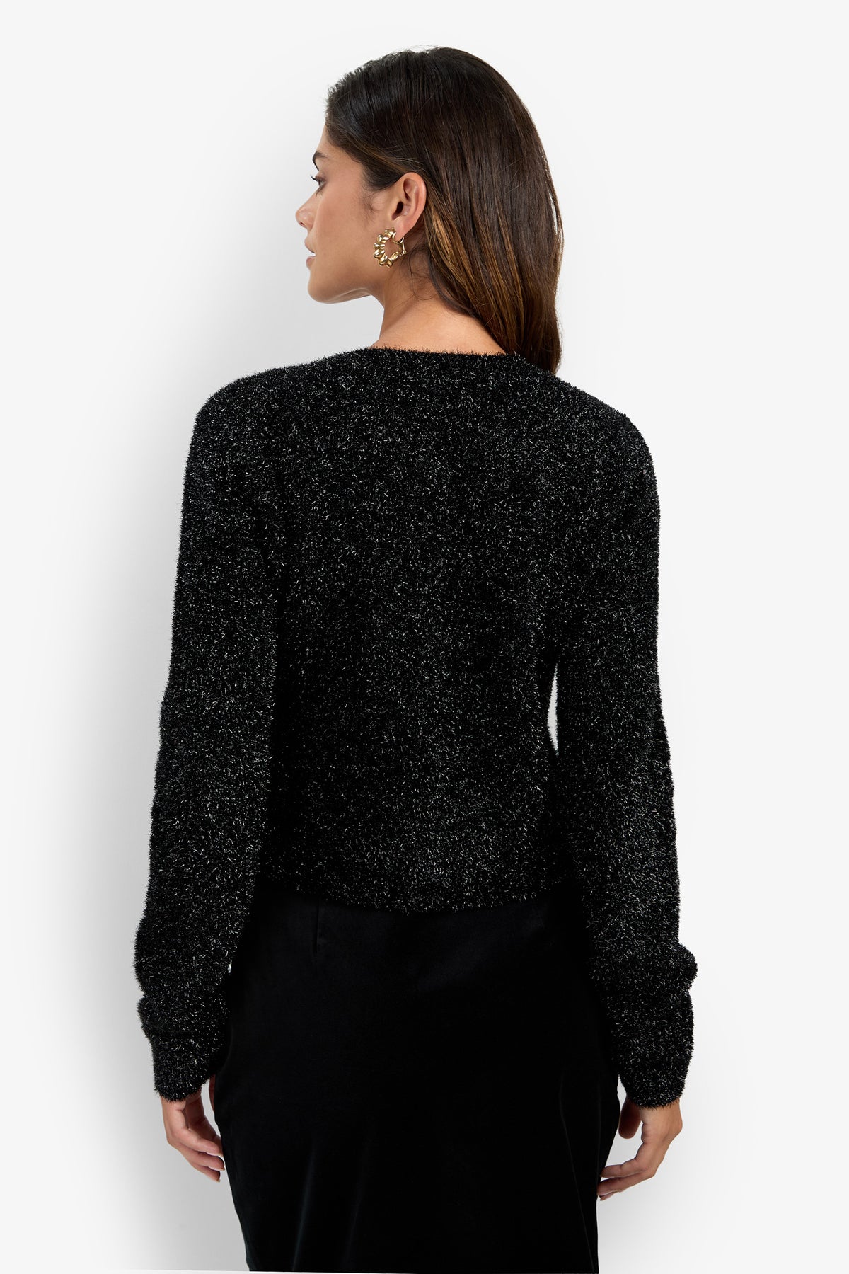 A woman with long brown hair wears the Sinai Cardigan, a fuzzy black sweater, paired with a black skirt as she stands with her back to the camera against a plain white background.