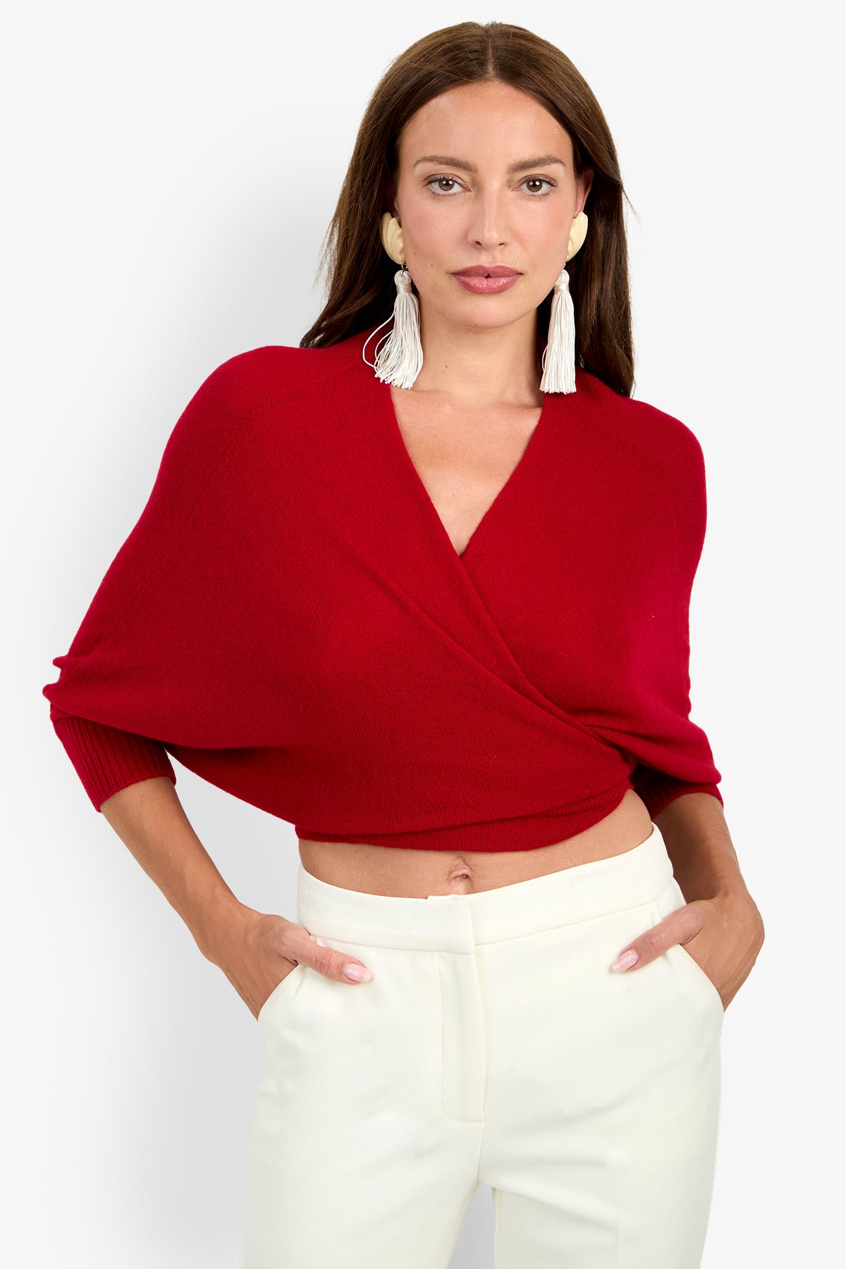 A person wearing a cropped red cashmere FLORENTINA WRAP sweater with wide sleeves and white trousers.
