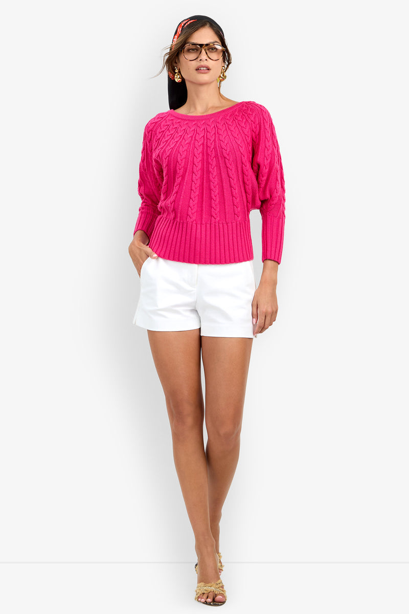 A person wearing a bright pink Tyson Knit Sweater with a boat neckline and white shorts.