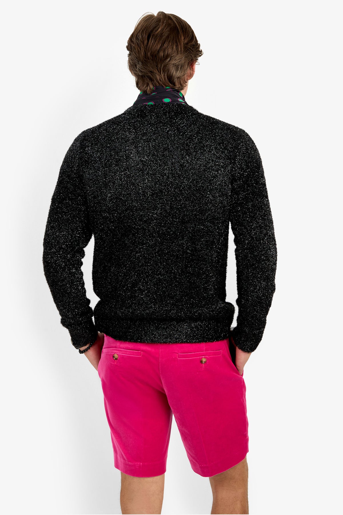A person stands facing away, wearing the ASTRON SPARKLE CREWNECK in black with bright pink shorts and hands in pockets, against a plain white background.