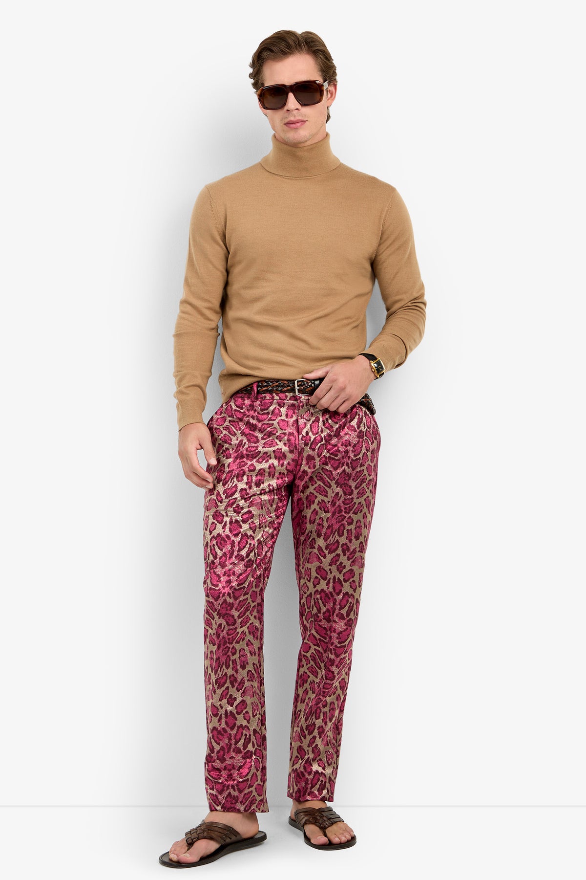A man wearing sunglasses, the WOODROW TURTLENECK in tan, pink leopard print pants, a black belt, and flip-flops stands against a white background.