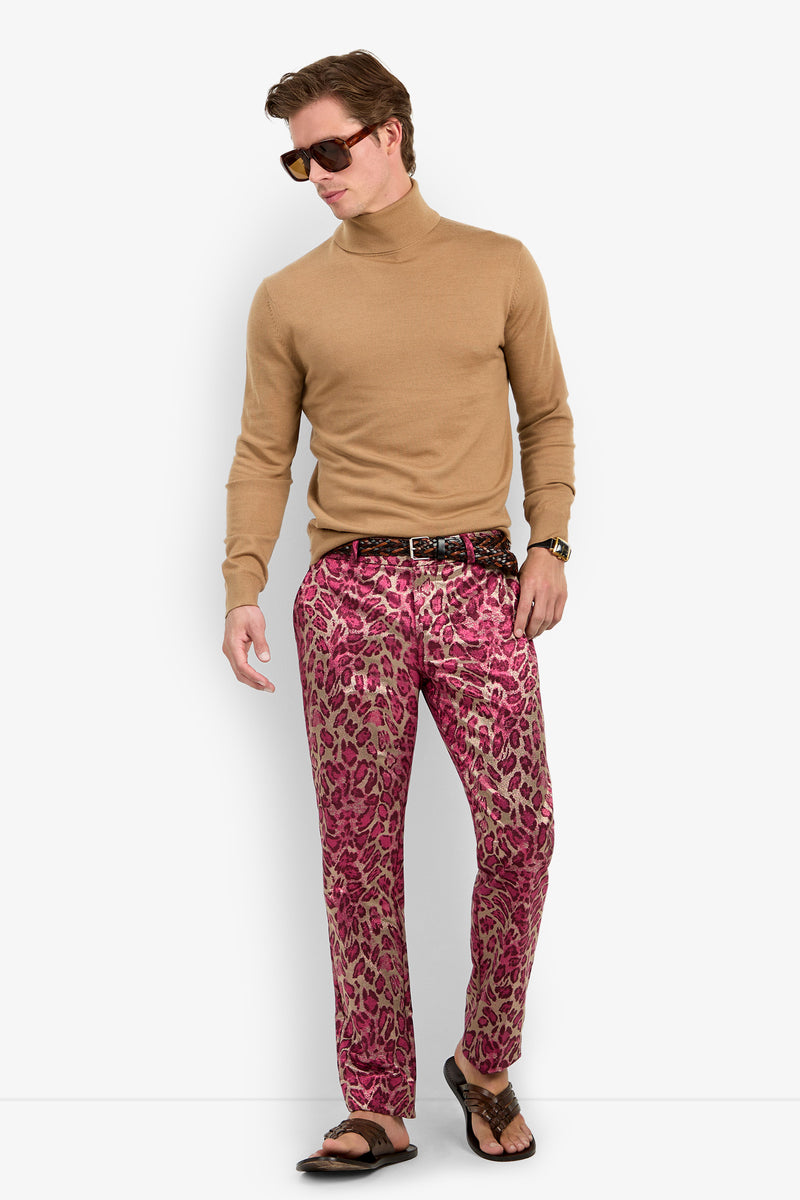 A man wearing sunglasses, the WOODROW TURTLENECK in tan, pink leopard-print pants, a dark belt, and sandals stands against a white background, looking slightly to his left.
